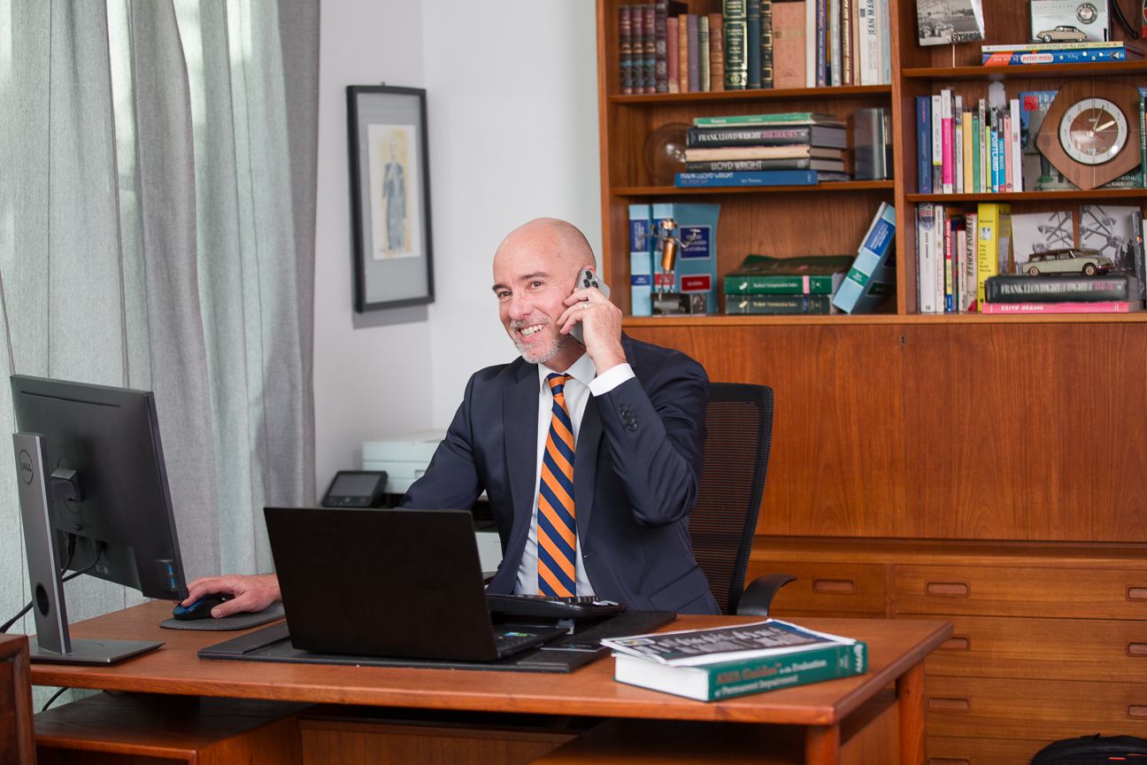 Executive office interior with wooden bookshelves, American flag, and person working at desk.