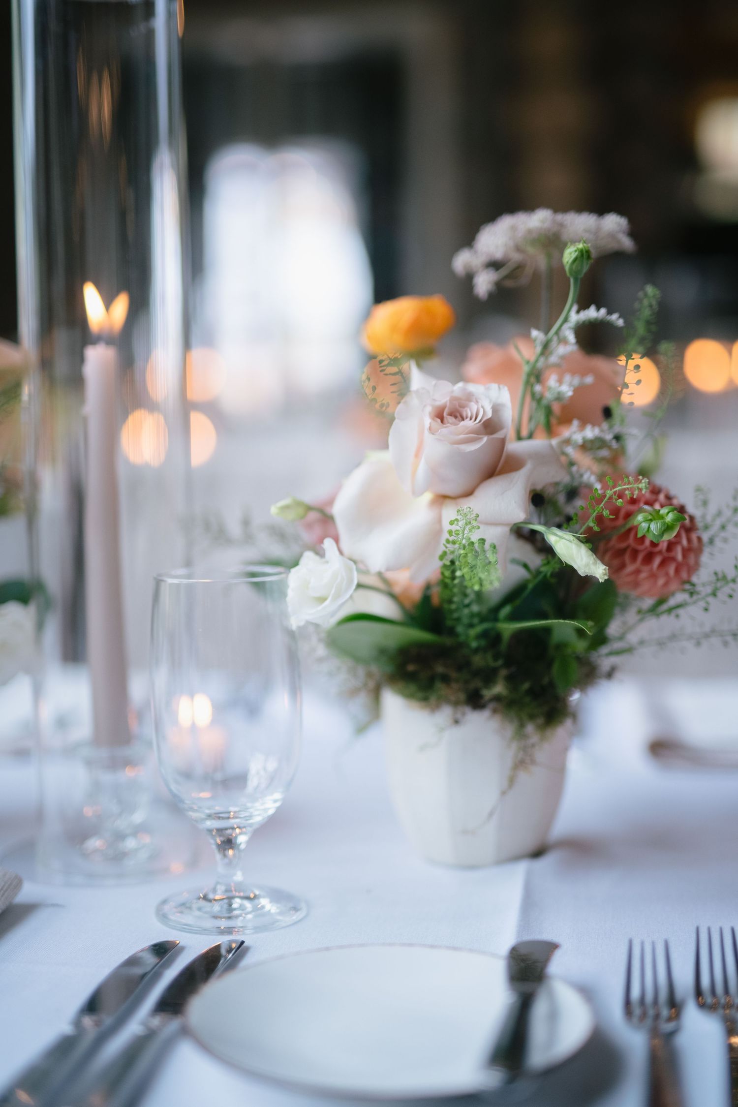 Elegant table setting with pink roses and glassware in soft lighting.
