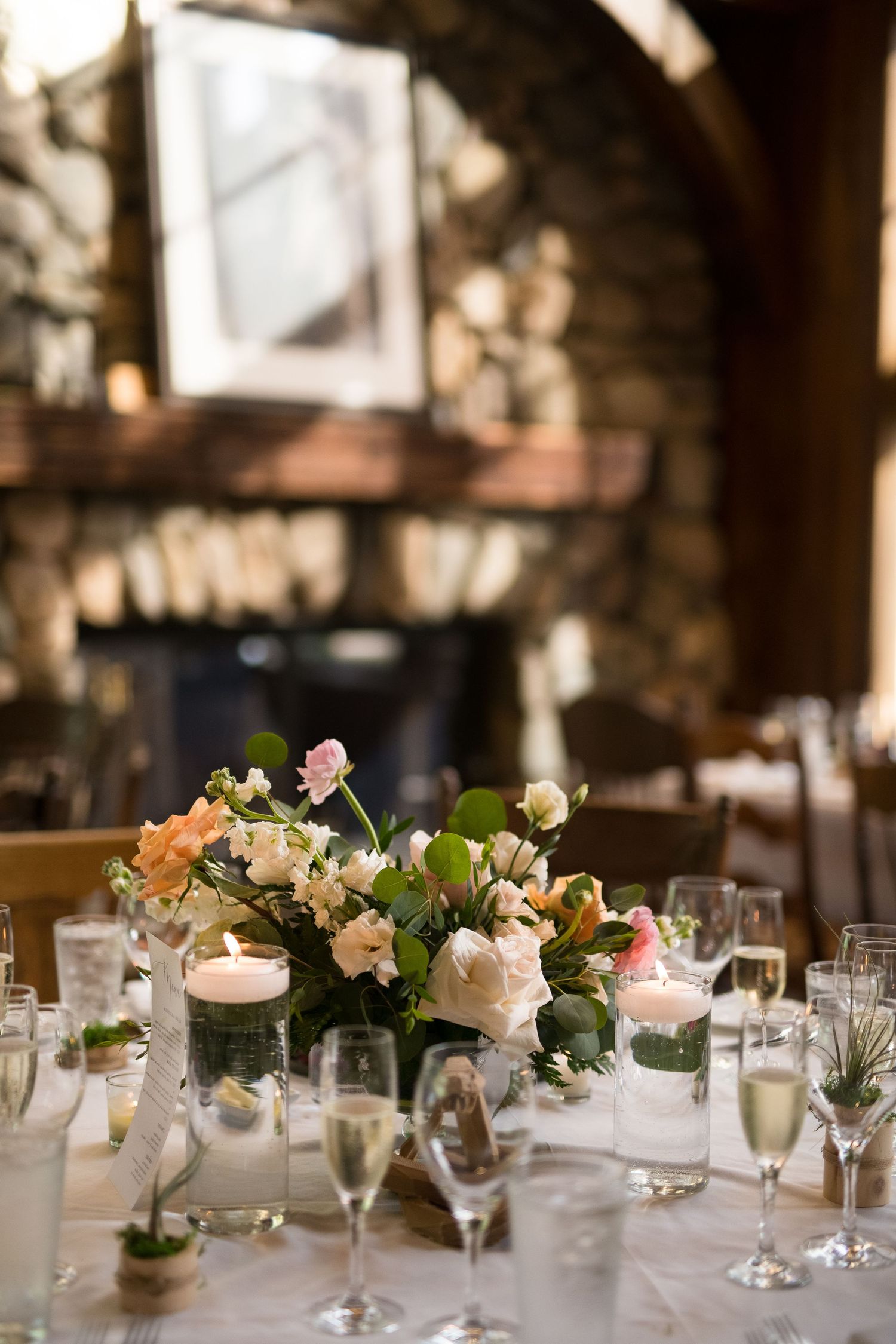 Elegant wedding reception table with floral centerpiece of white and pink roses, candles, and champagne glasses in a rustic venue.