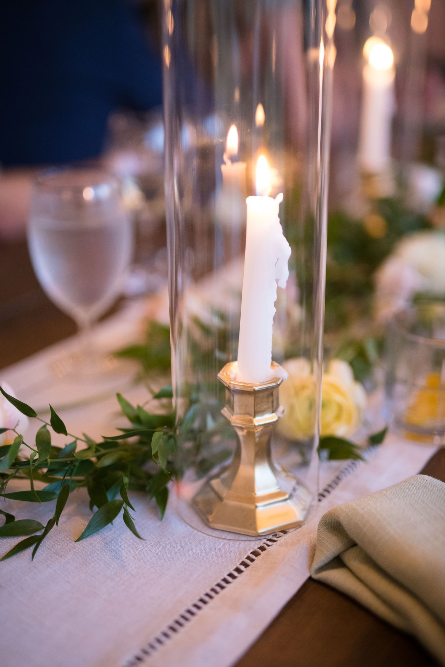 Elegant table setting with glass hurricane candle holders and greenery garland.