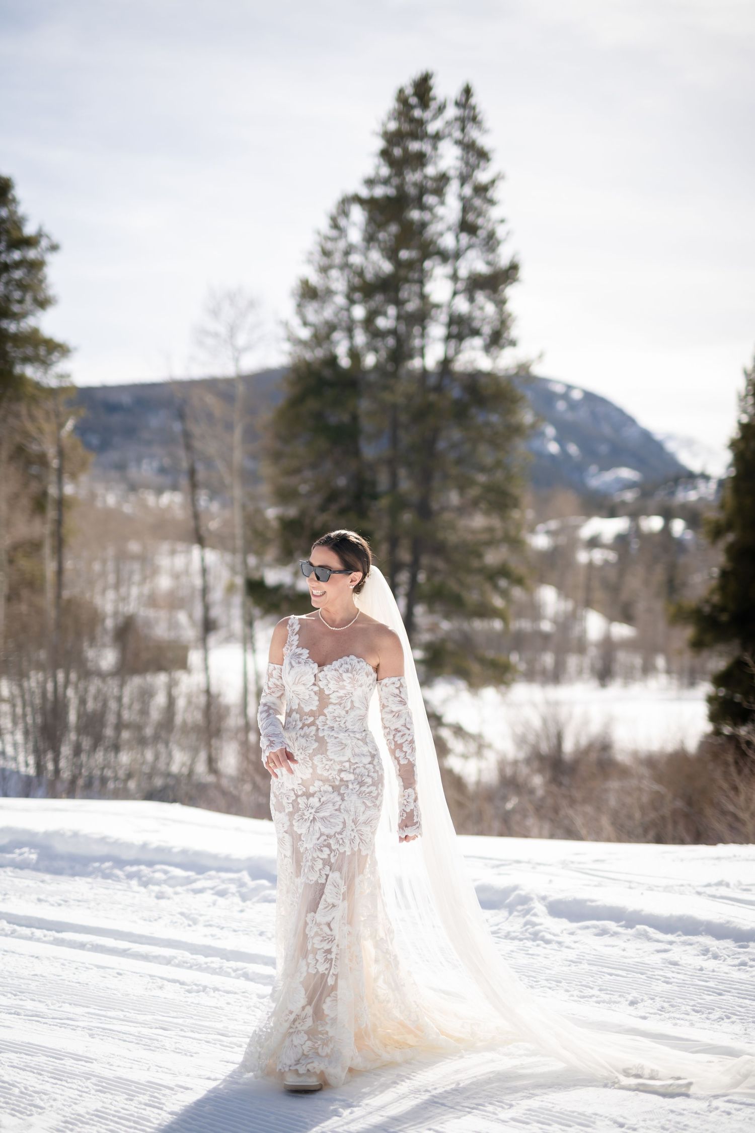 An elegant wedding dress sparkles in the winter sunlight against snow-covered mountains.
