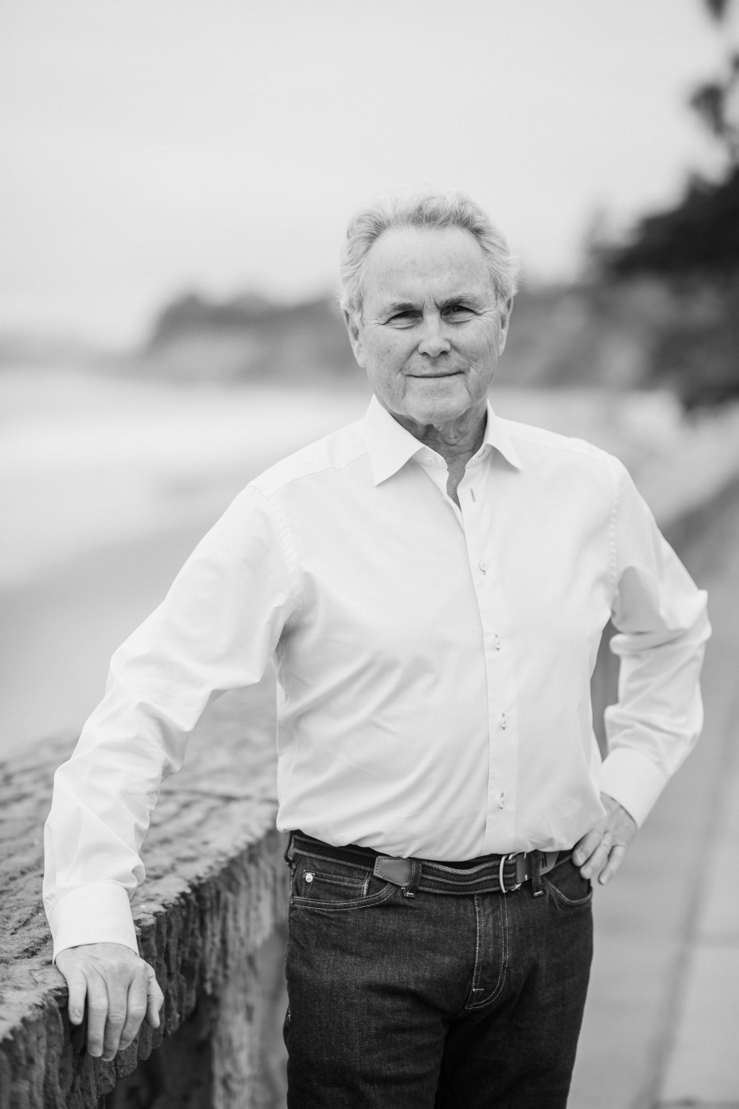 A casual portrait of someone in a white button-down shirt standing outdoors near a beach.