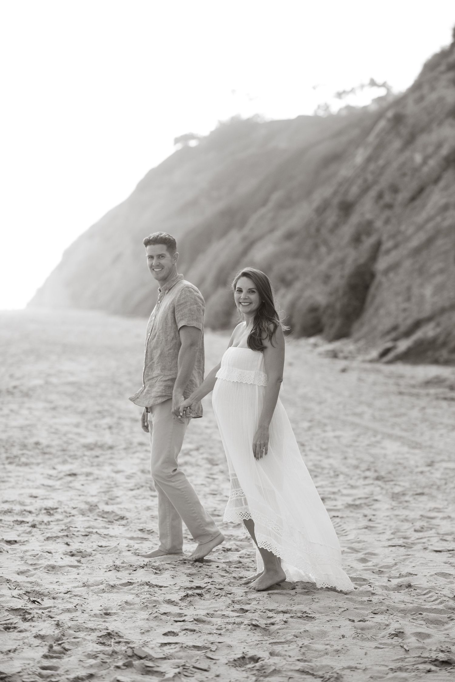Couple walking and playing on misty beach in casual attire.
