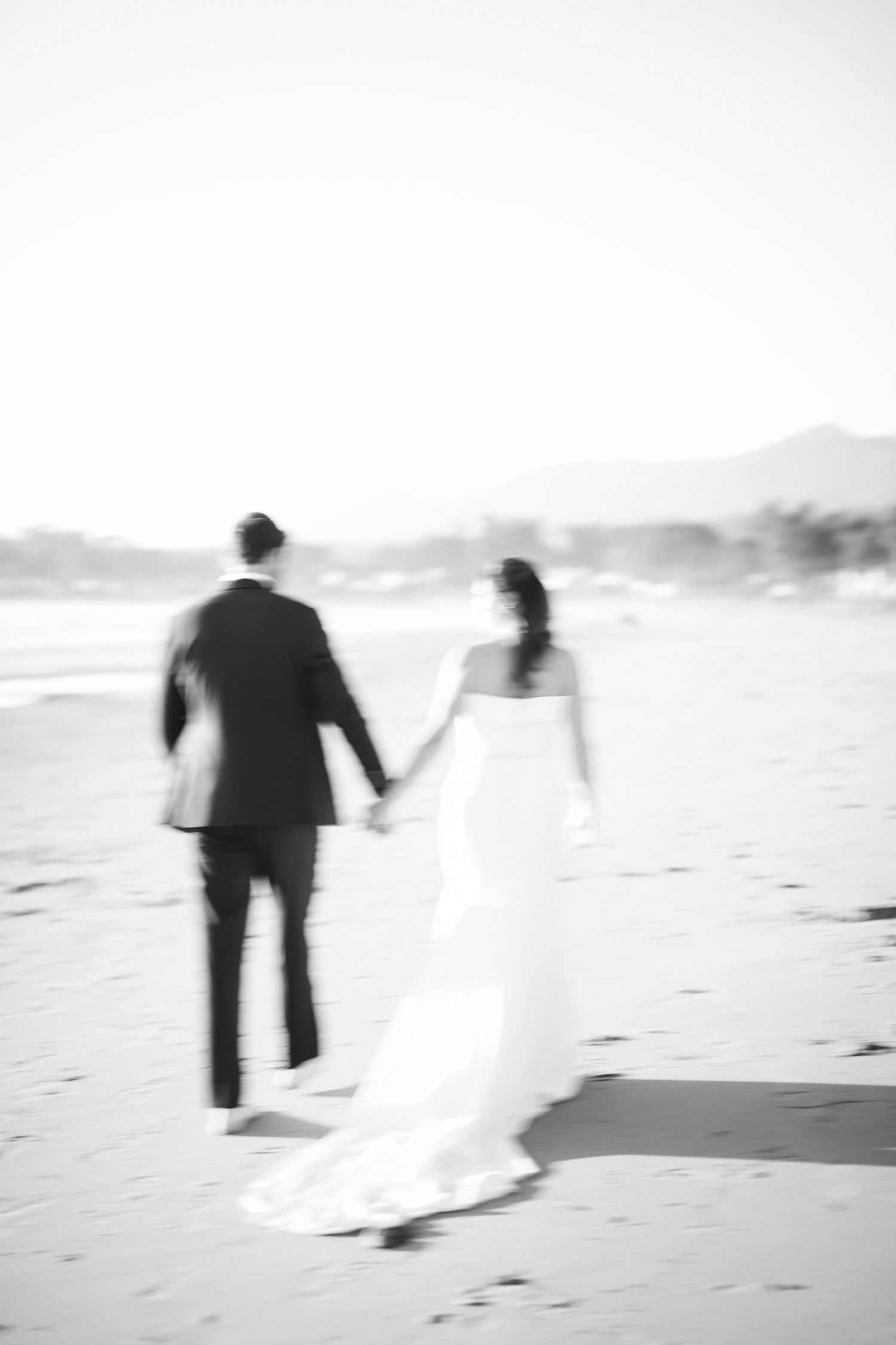Blurred black and white image of couple walking hand in hand on beach.