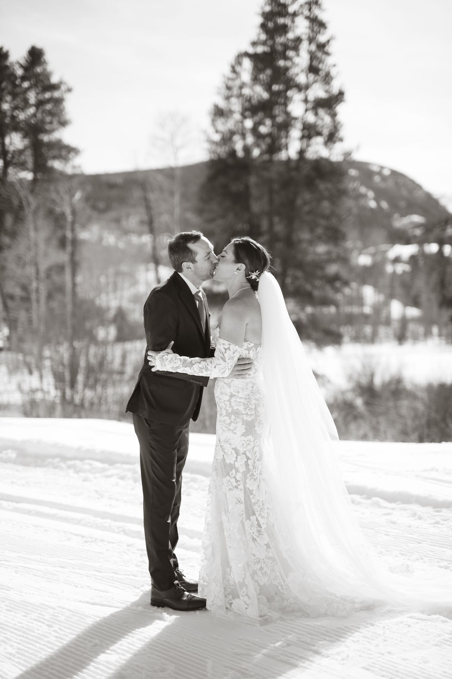 Black and white winter wedding photos on snowy terrain with mountain backdrop.