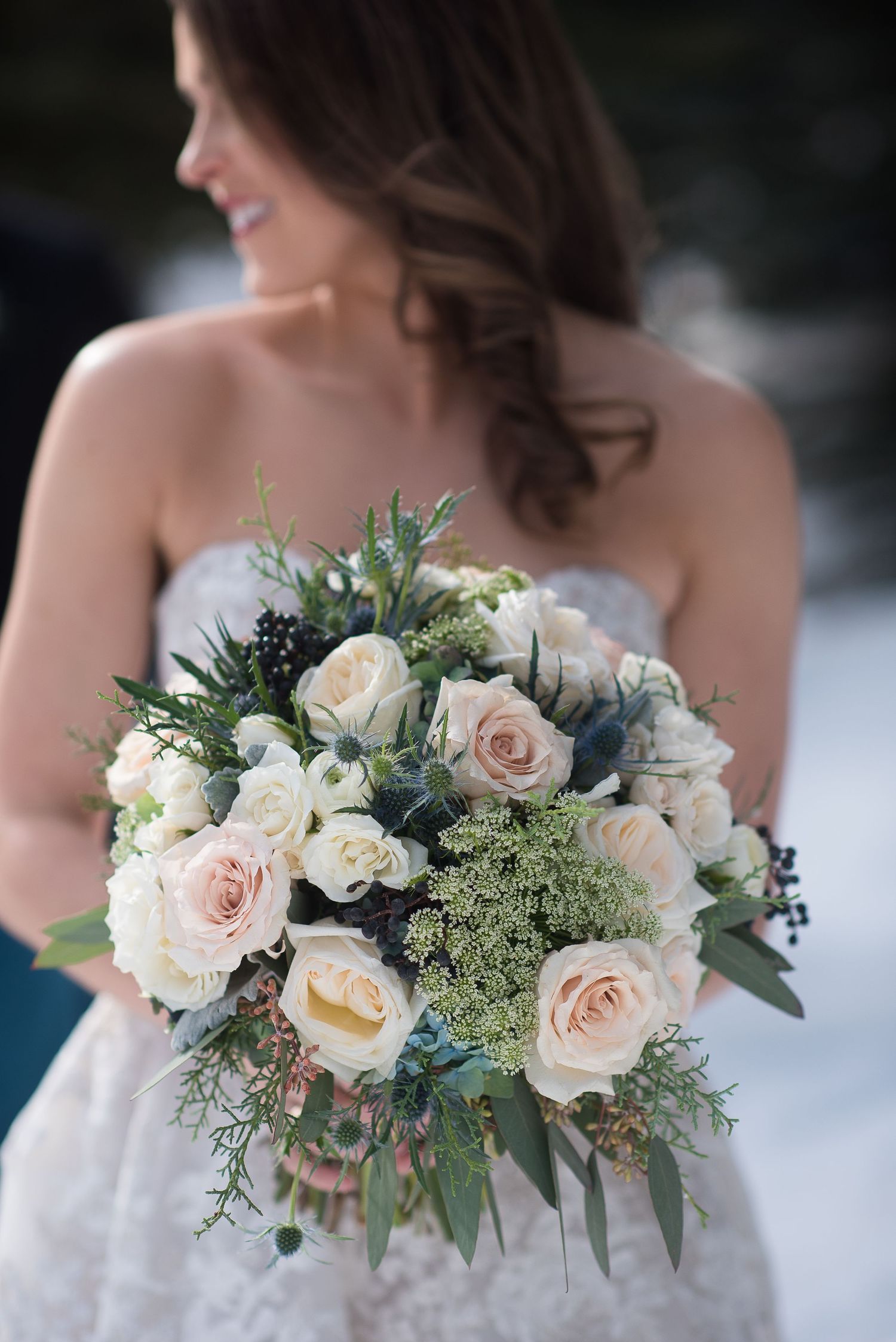 Elegant bridal bouquet featuring blush roses, white flowers, and greenery against snowy background.