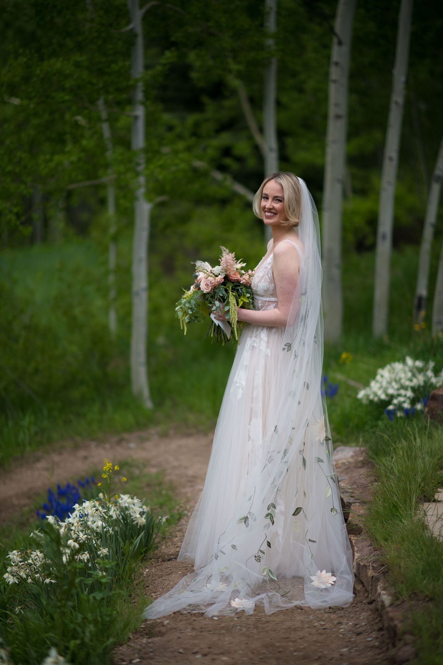 A white wedding dress and veil photographed in an aspen grove with wildflowers.