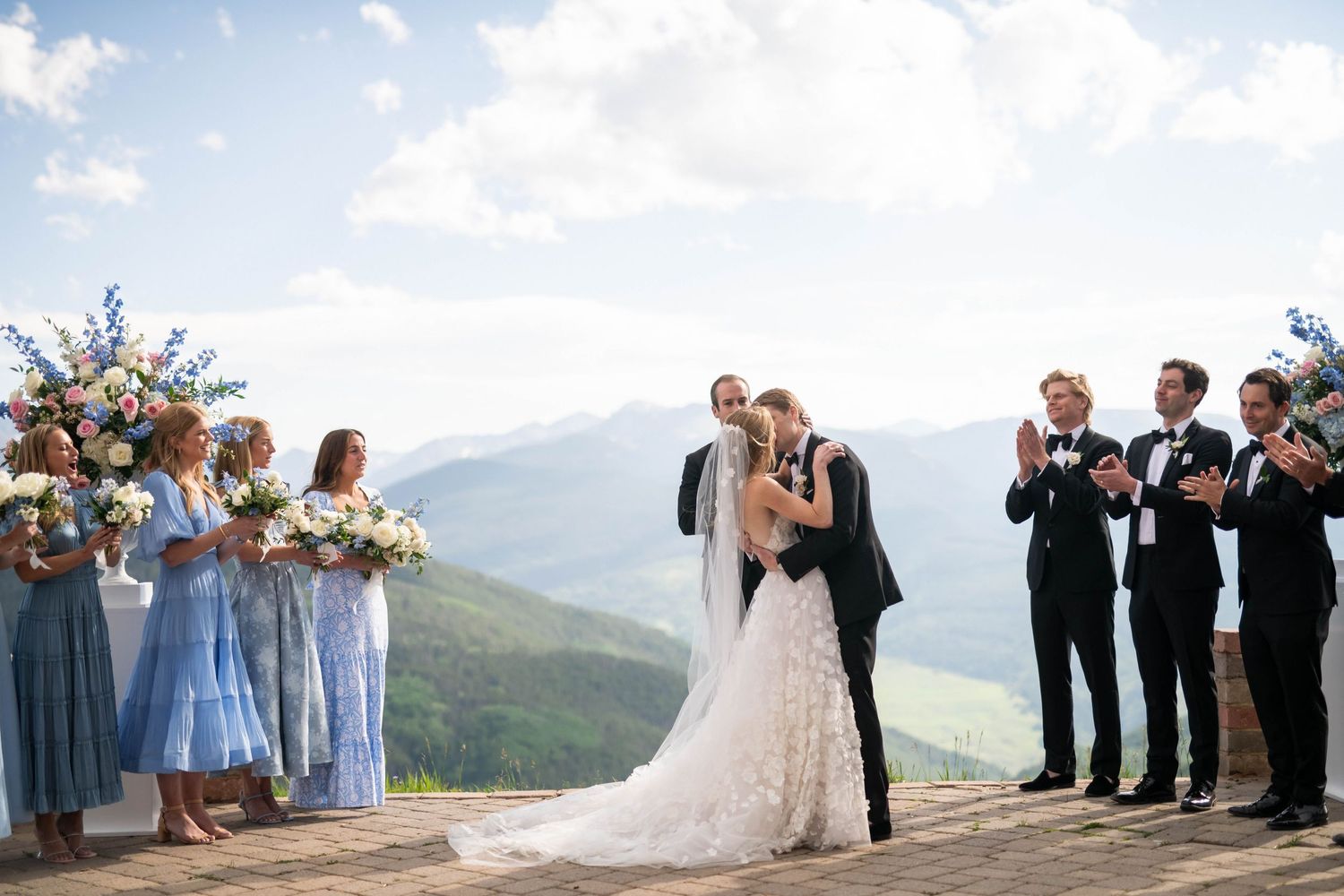Scenic mountain wedding ceremony with blue-clad wedding party against dramatic landscape.