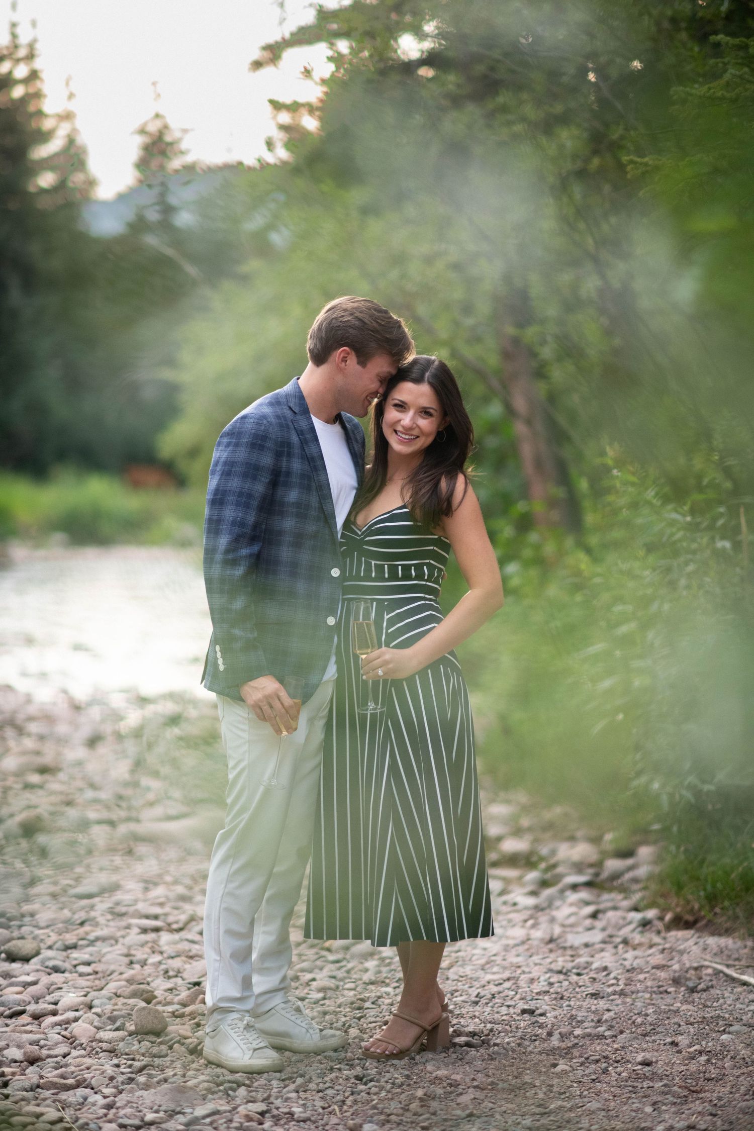 A couple shares playful moments on a rocky riverbank surrounded by misty forest.