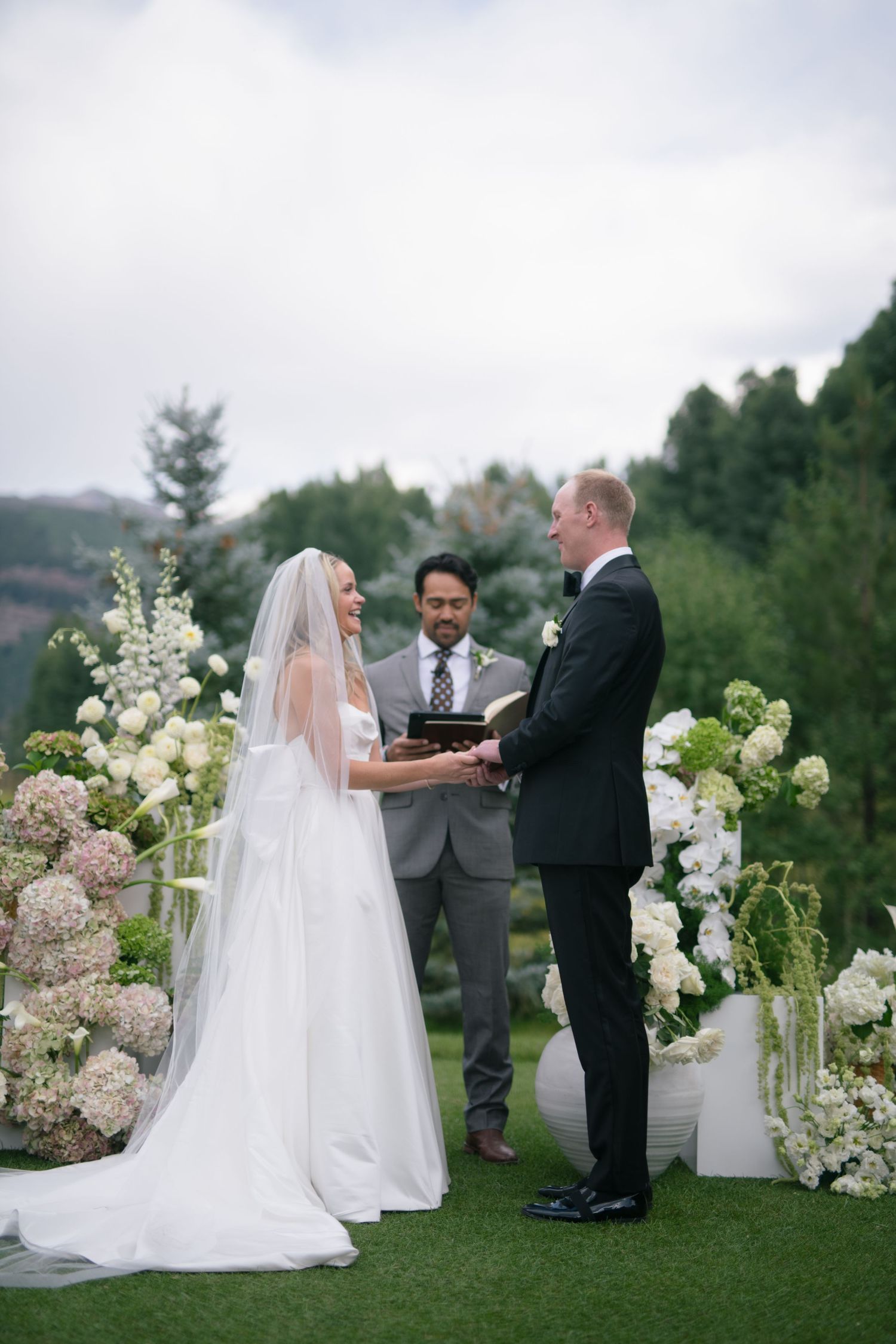 A garden wedding ceremony with white floral decorations and mountain views in the background.