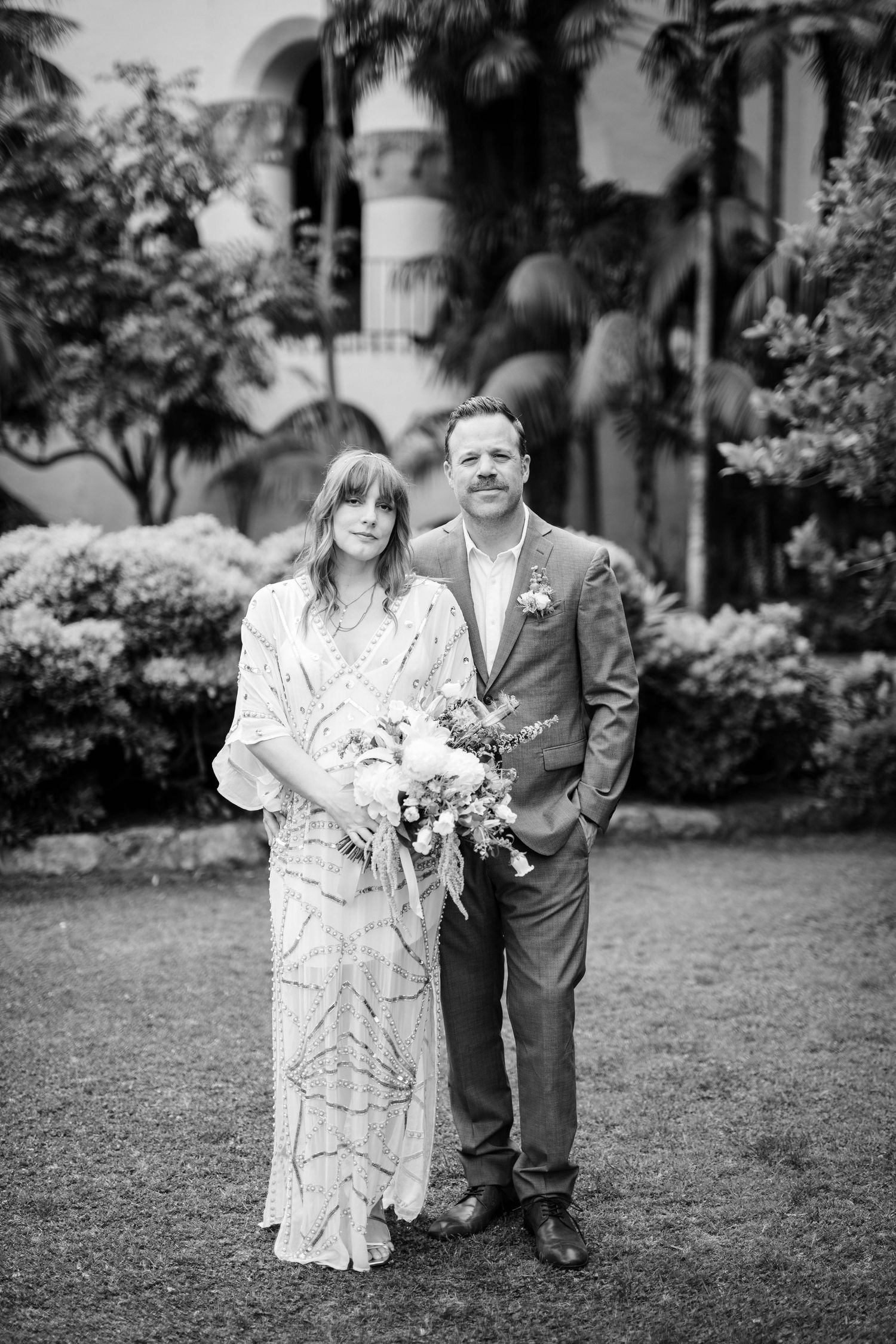 Black and white wedding portraits taken in a garden setting with classic architectural elements.