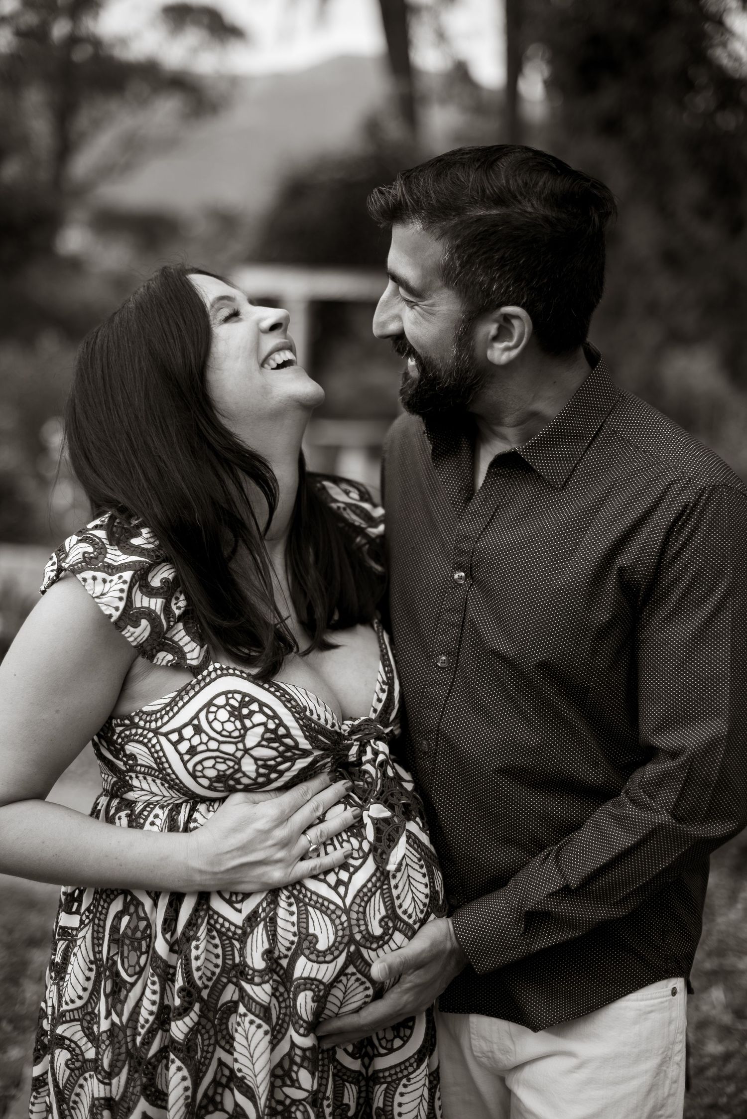 Black and white maternity photo session with couple laughing together.