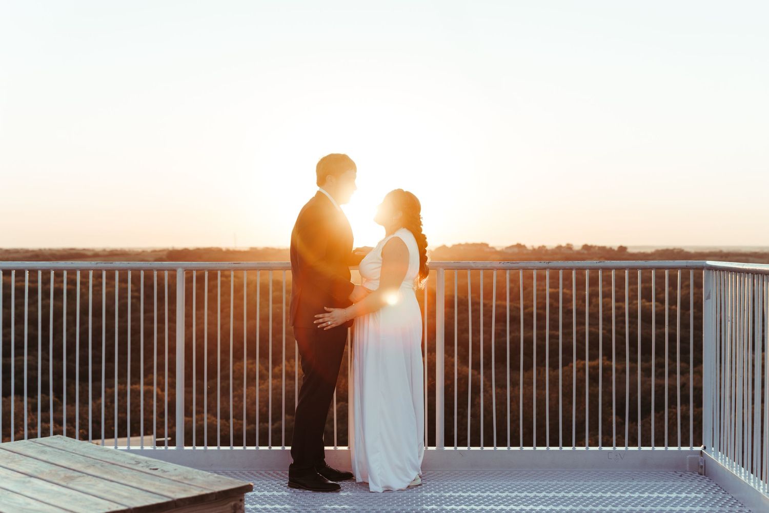 A couple stands silhouetted against a golden sunset on a pier overlooking the ocean with dramatic lighting.