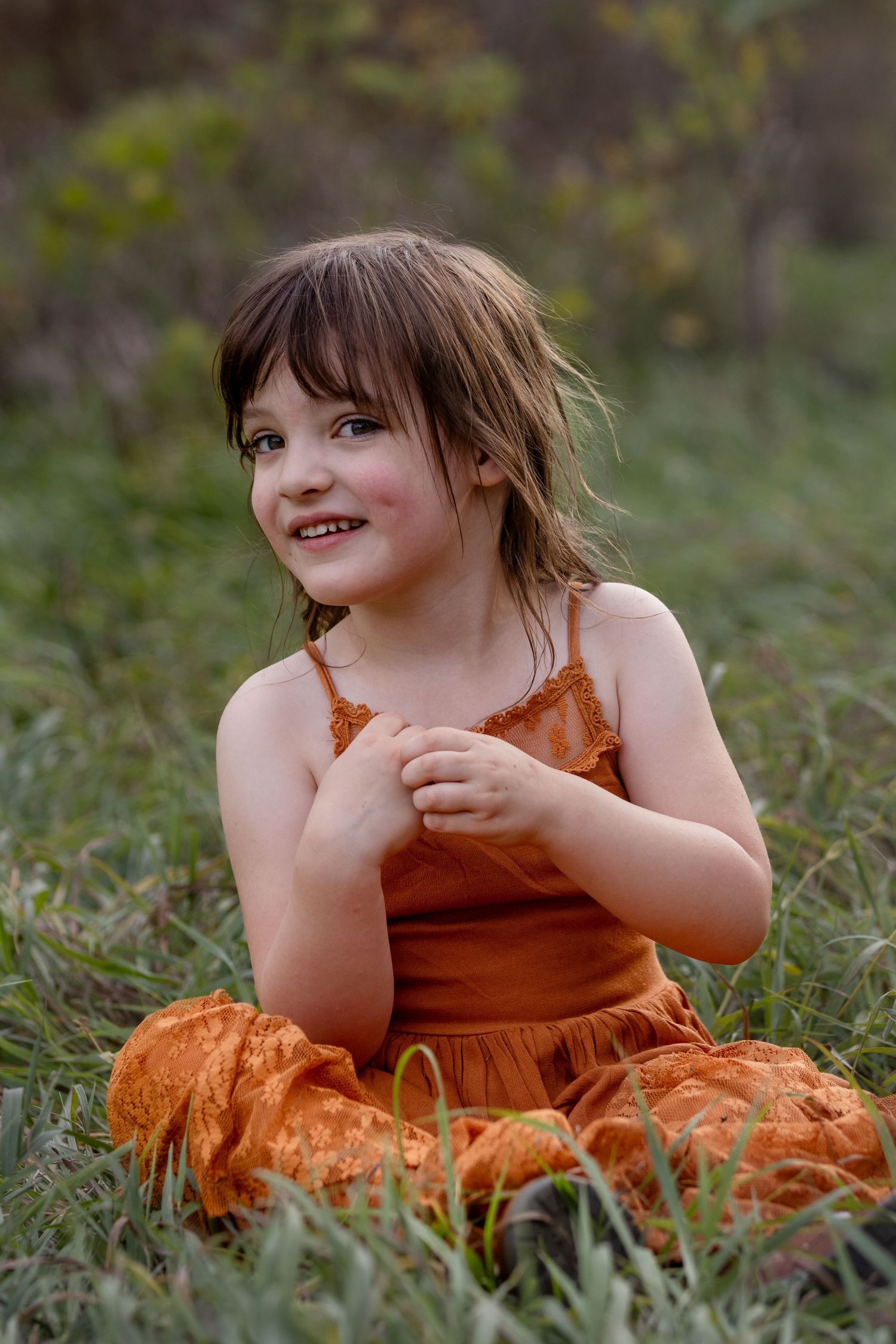 Child in orange dress sitting in grass with natural lighting.