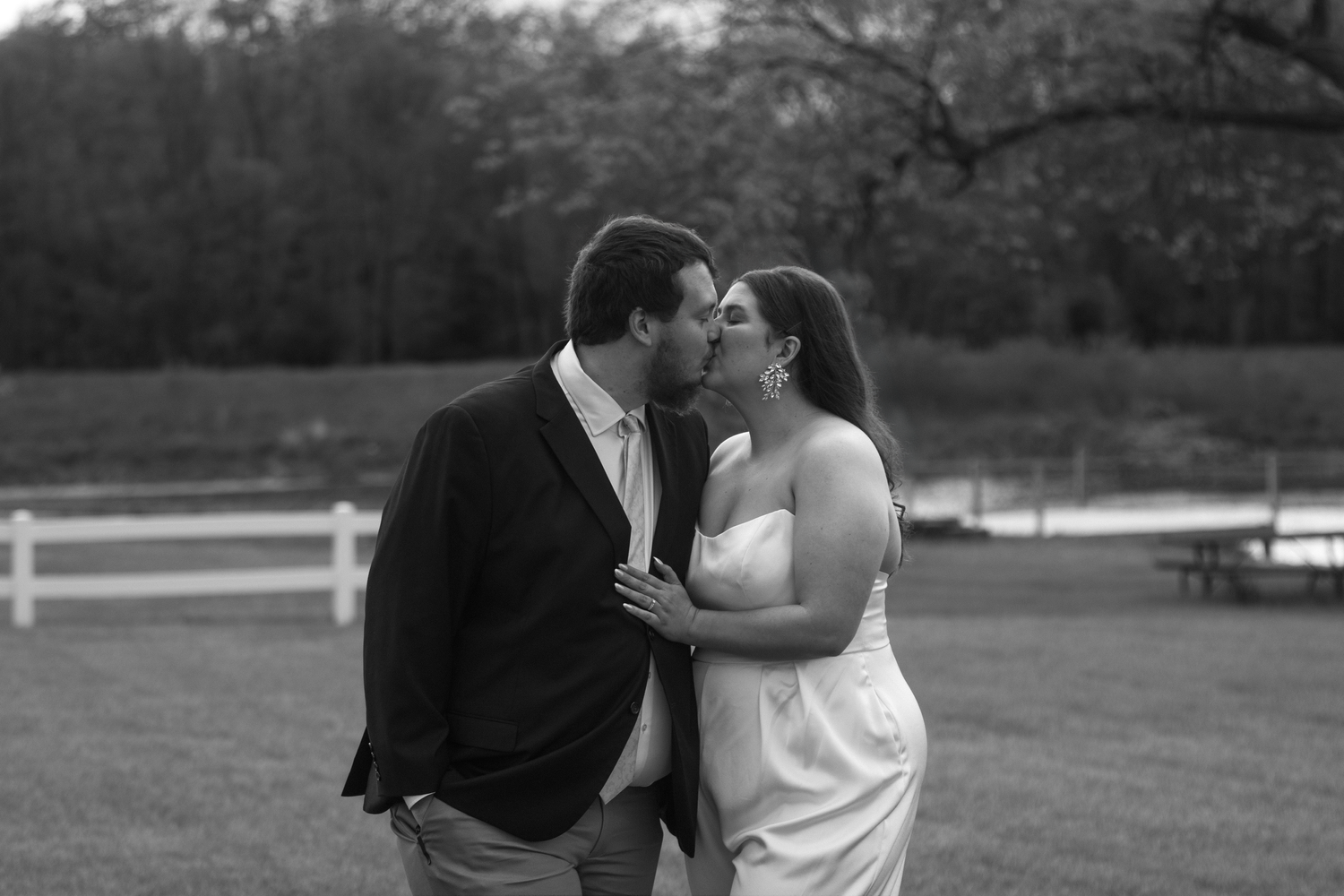 Romantic black and white engagement photo of couple in formal wear on grassy field.