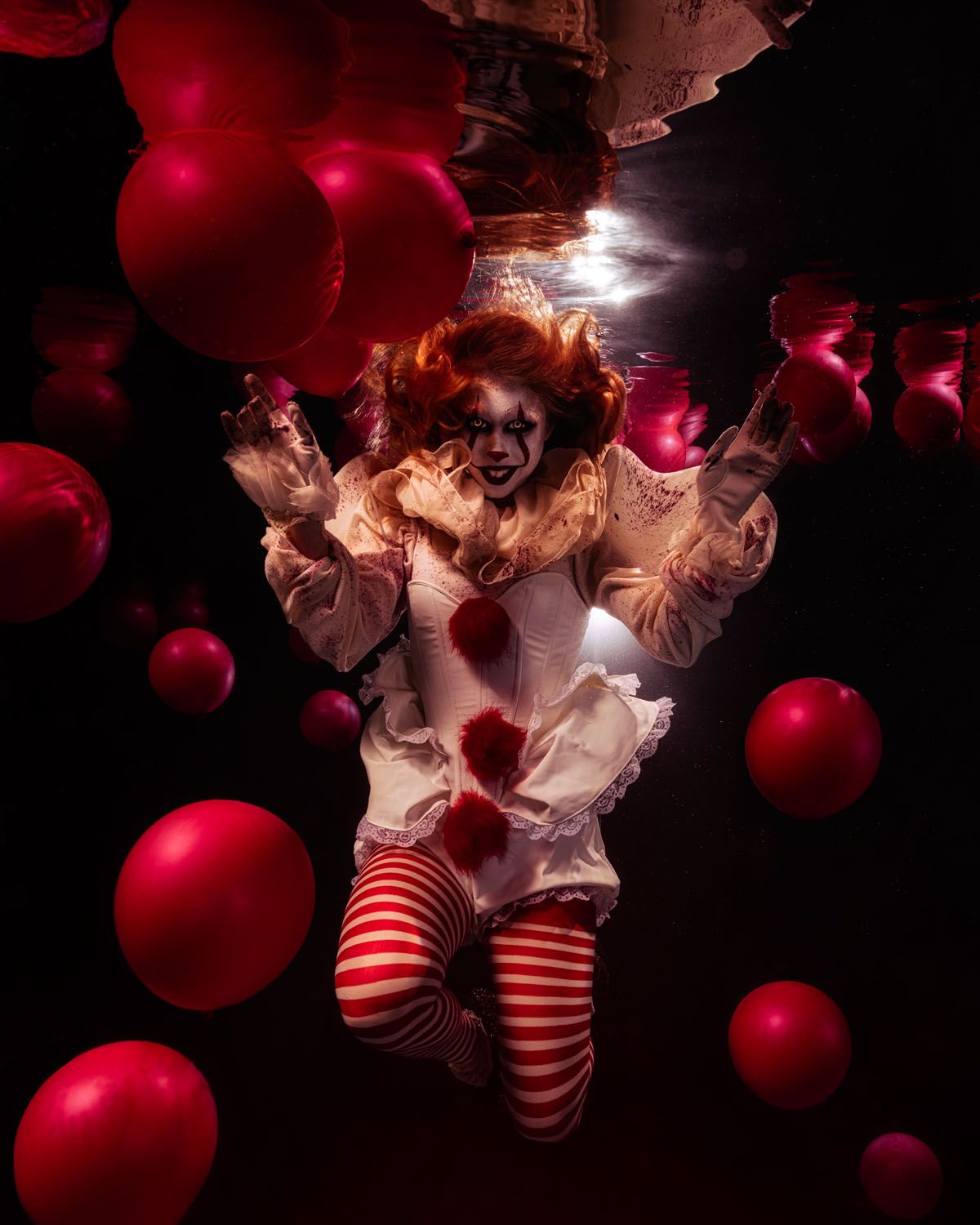 Dark artistic scene with person in clown-like outfit and striped stockings surrounded by floating red balloons in moody lighting.