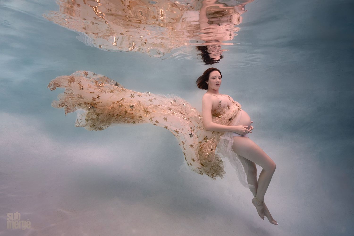 An ethereal underwater dance scene with flowing pink fabric creating graceful movement in cloudy blue water.