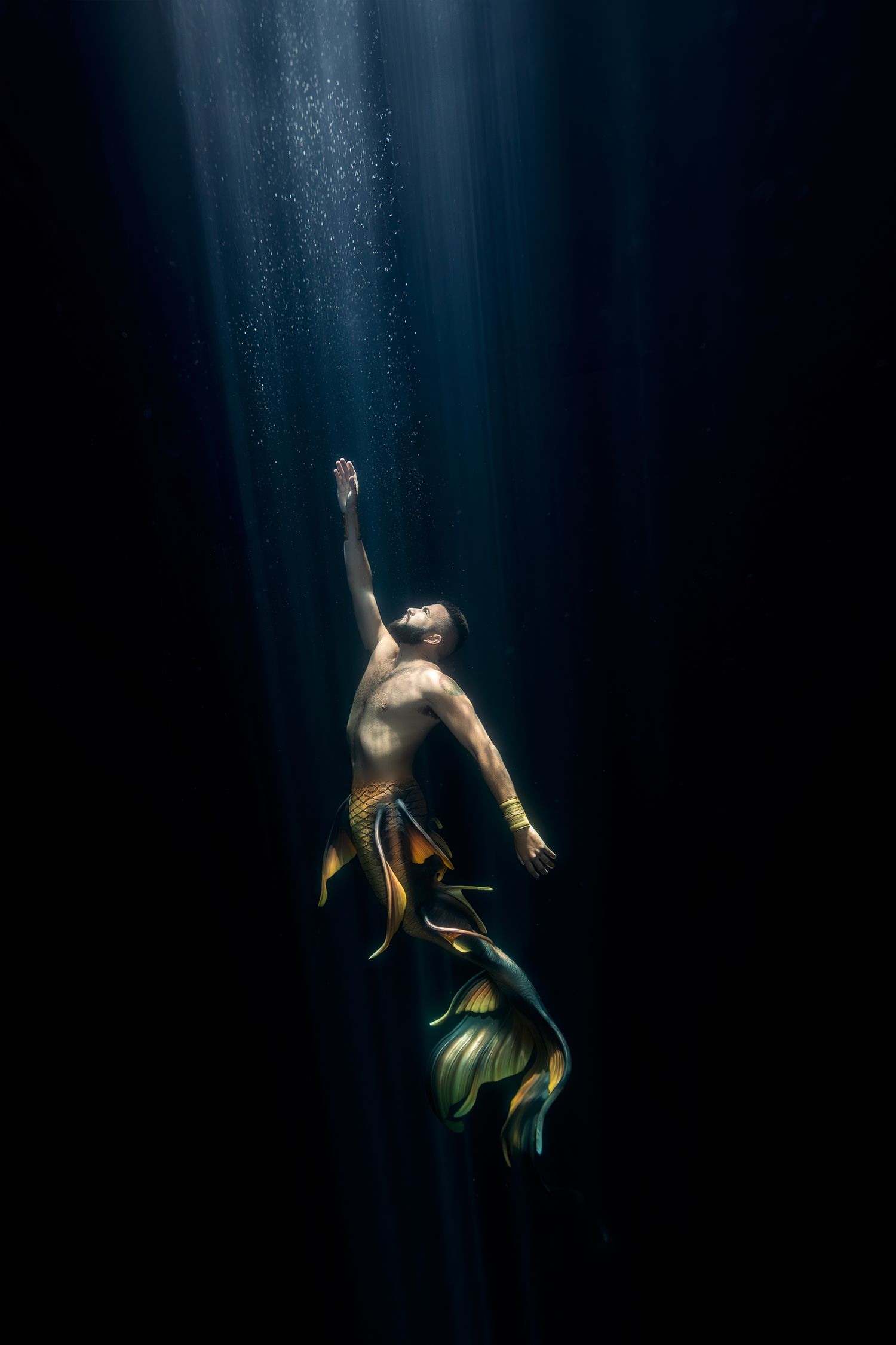 Dramatic underwater dance performance with figure reaching toward light beams in dark waters.