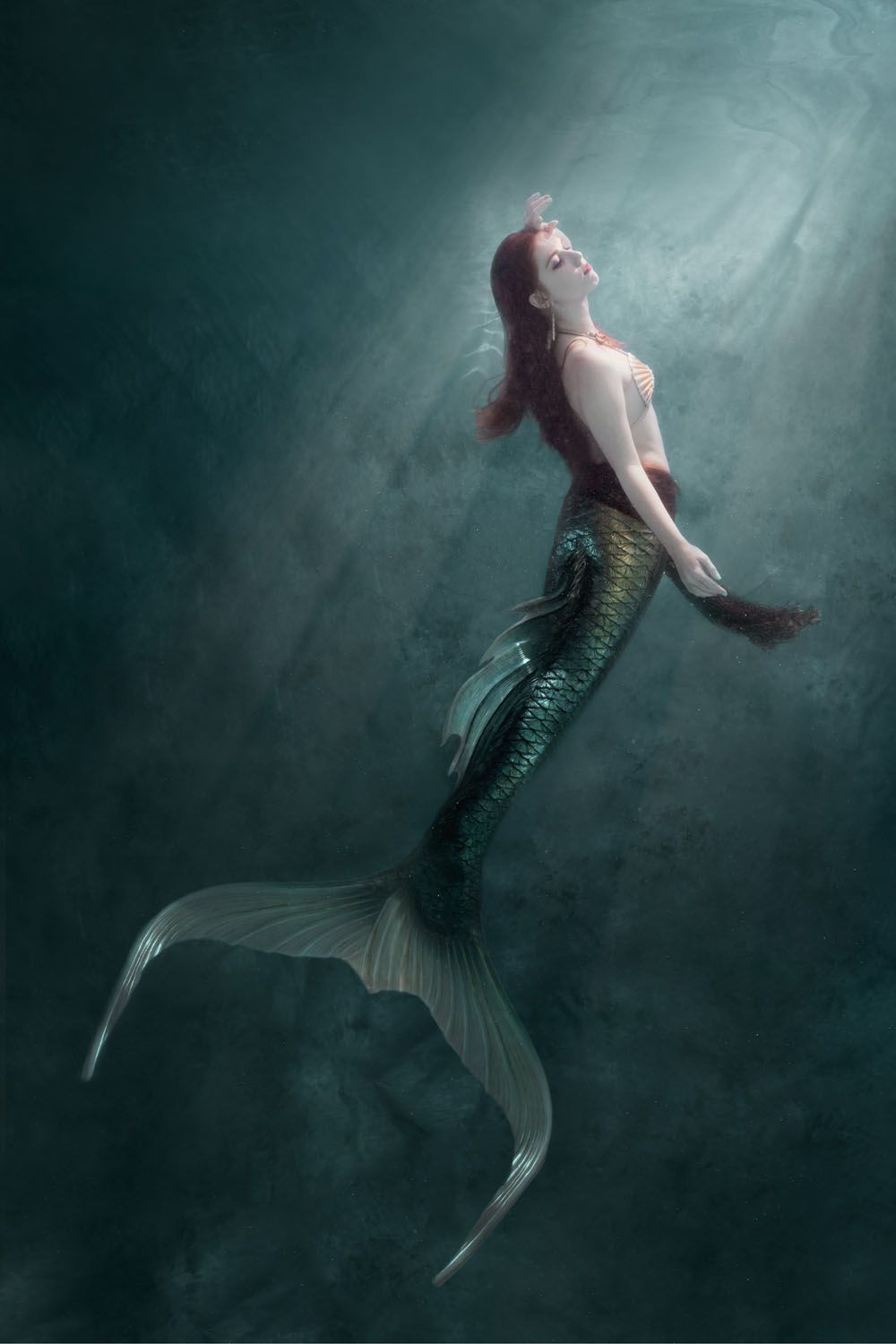 Artistic underwater portrait of mermaid floating in mystical green waters.