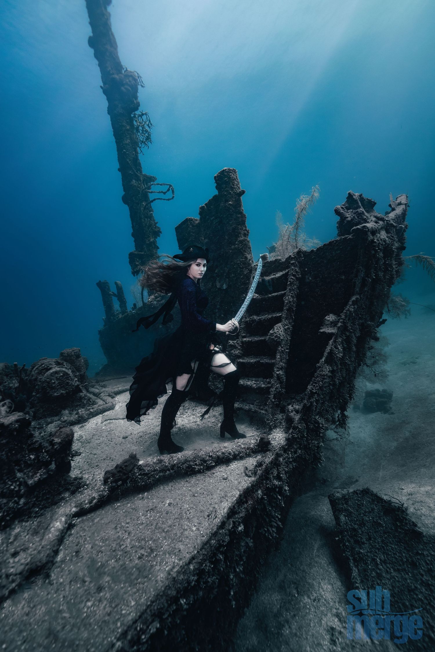 A scuba diver explores an eerie underwater shipwreck with beams of sunlight filtering through the deep blue water.