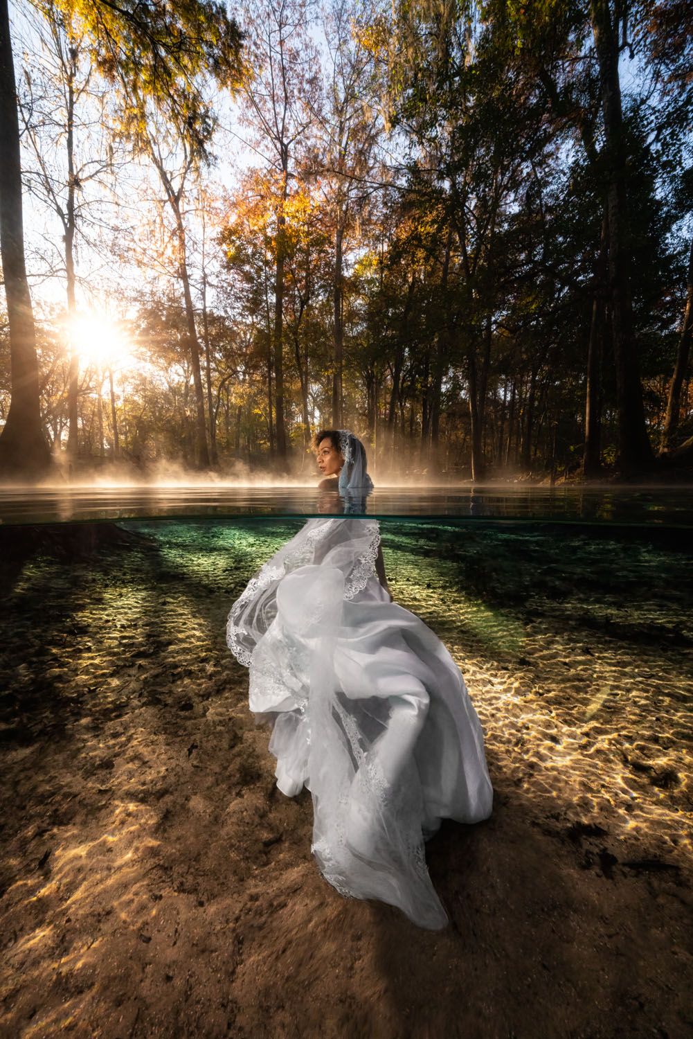 A flowing white dress billows in misty forest at sunset with golden sunlight streaming through autumn trees.