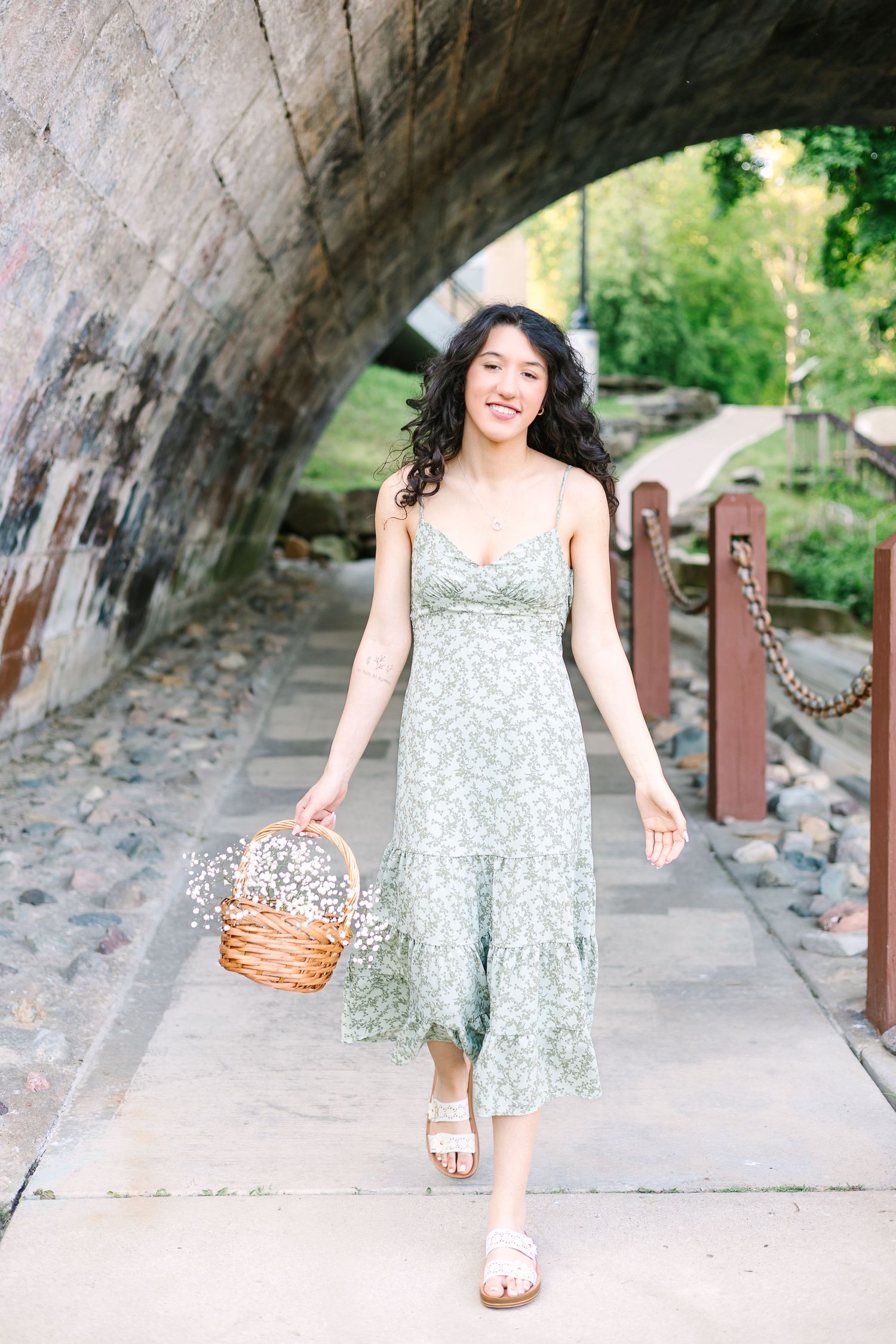 Multiple angles of someone wearing a floral print dress while walking under a stone bridge in a garden setting.