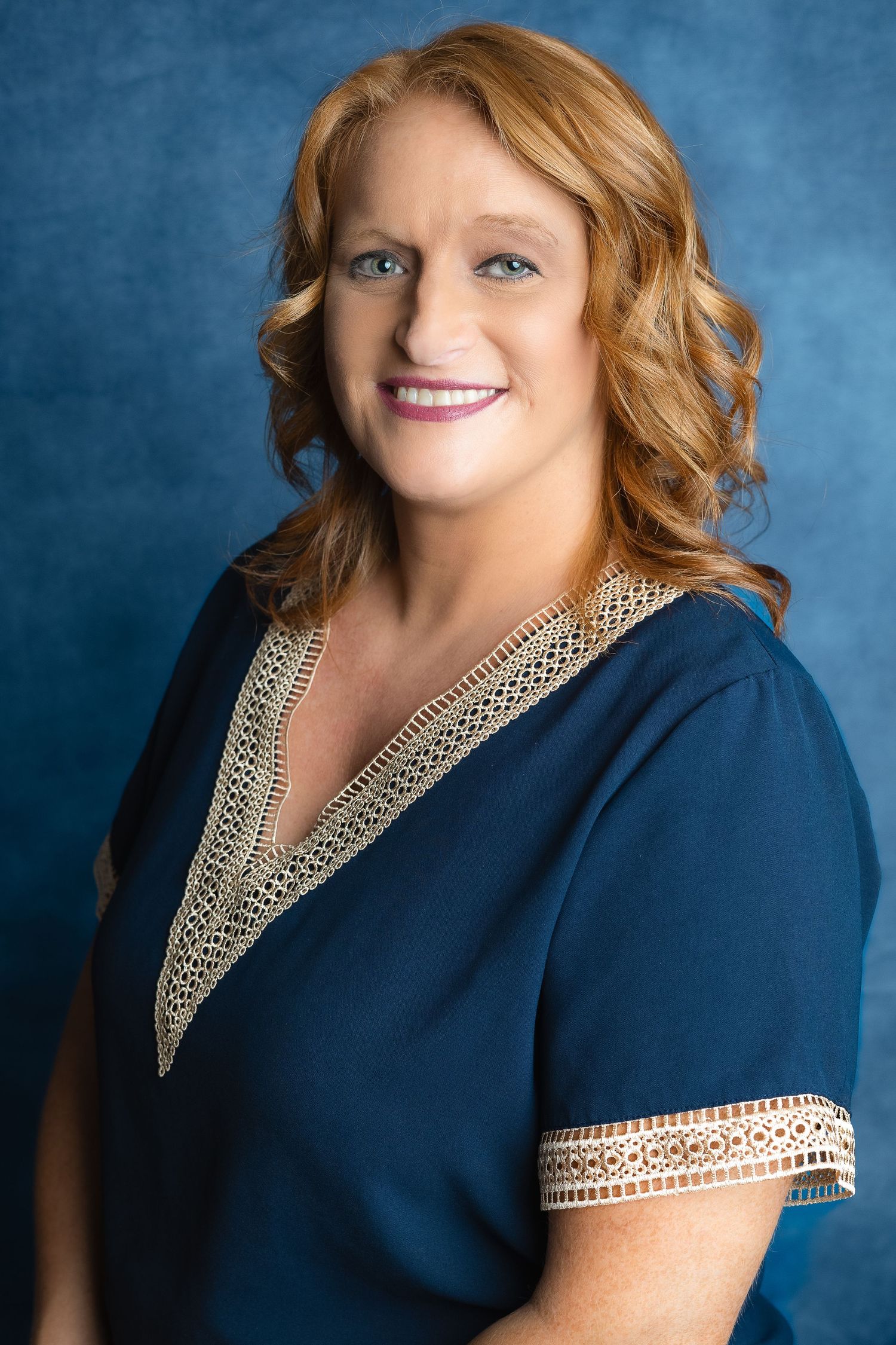 Professional portrait of someone in a navy blue dress with ornate gold trim against a blue backdrop.