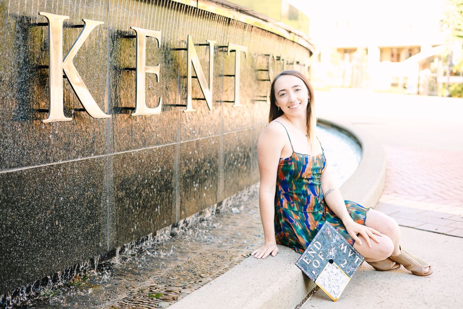 A musician sits casually by a wall with the text 'KENT' in a patterned dress during golden hour.