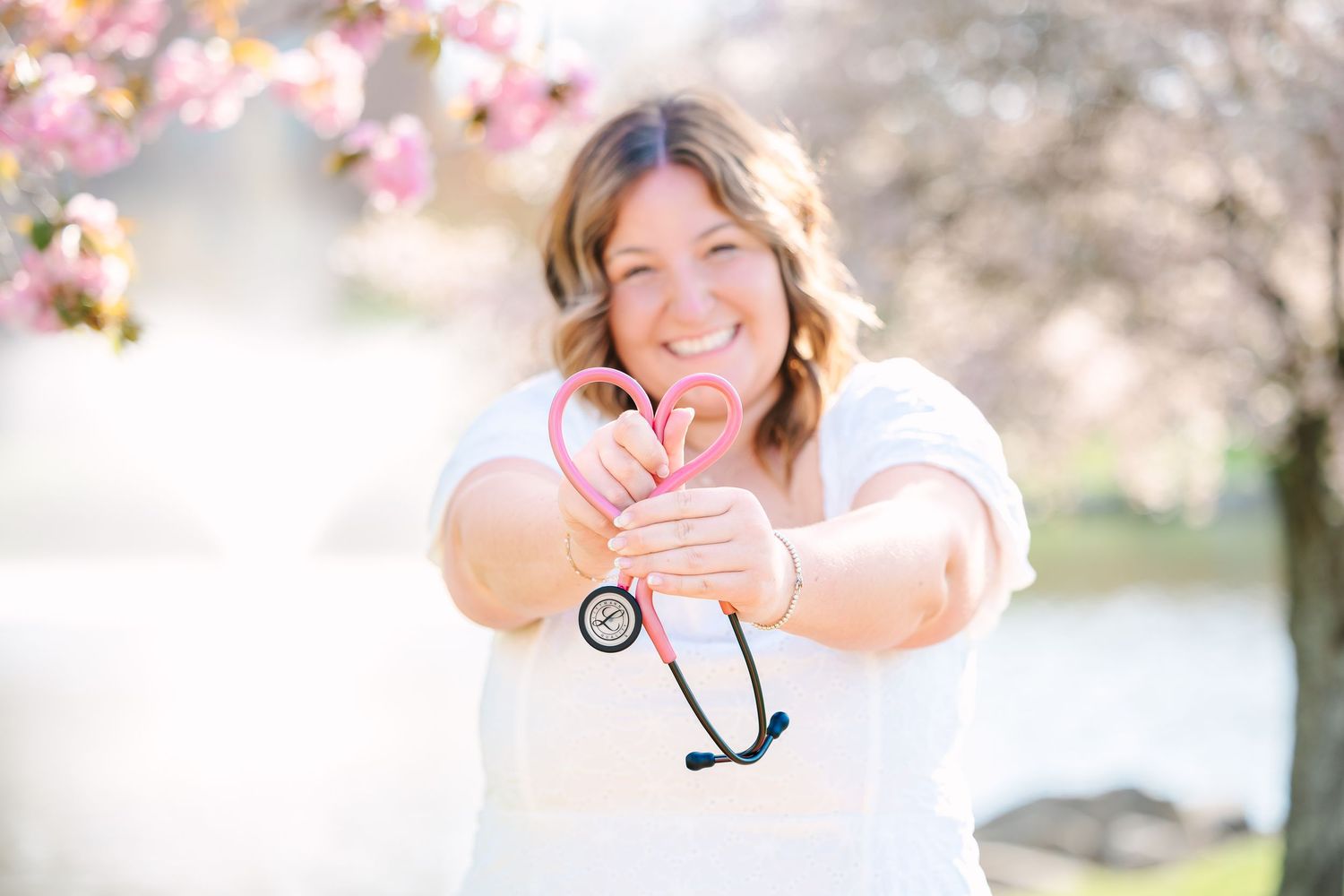 Healthcare professional holding a stethoscope amid blooming spring cherry blossoms in a sunny outdoor setting.
