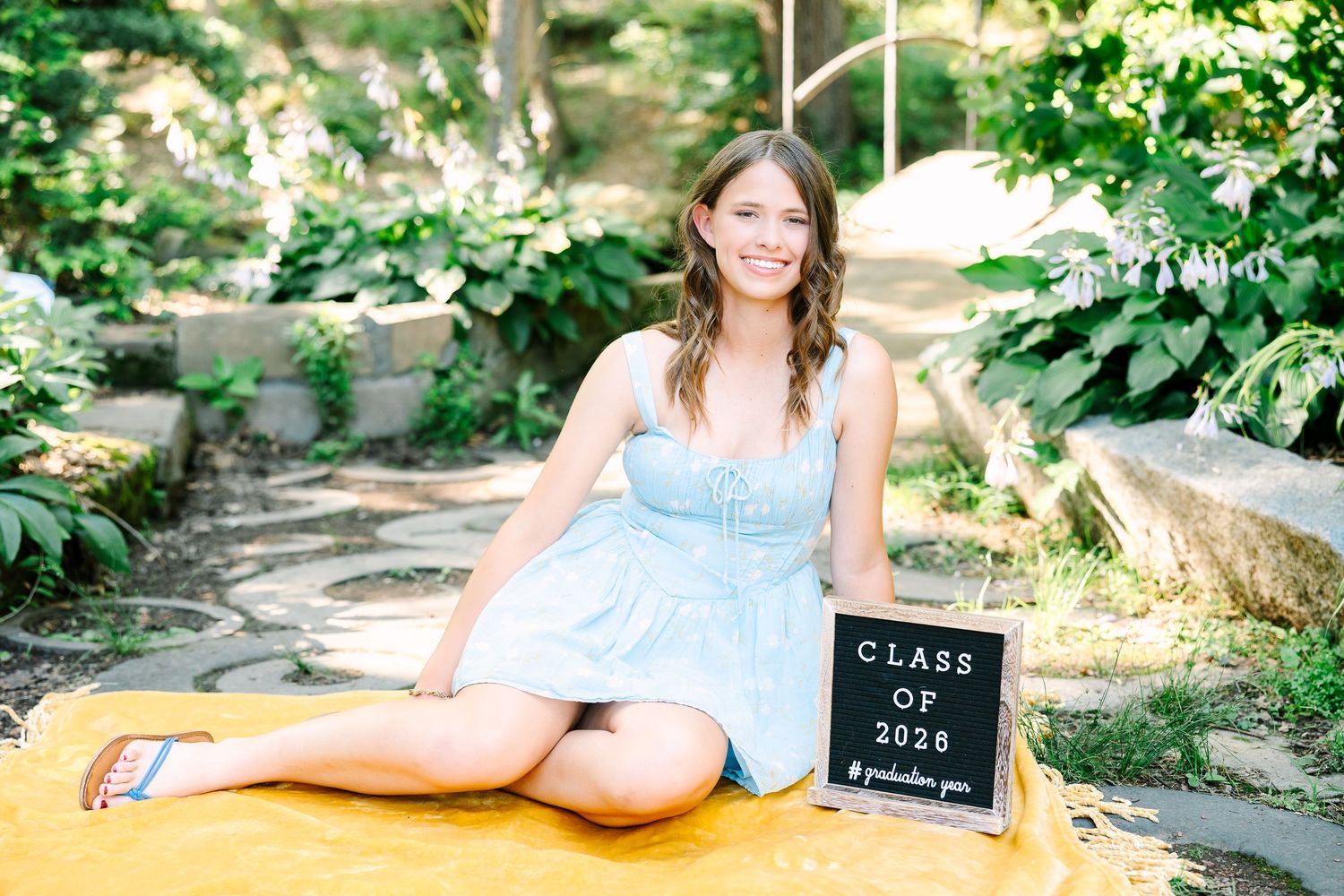 A graduation photo session in a lush garden setting with a chalkboard sign and casual summer attire.