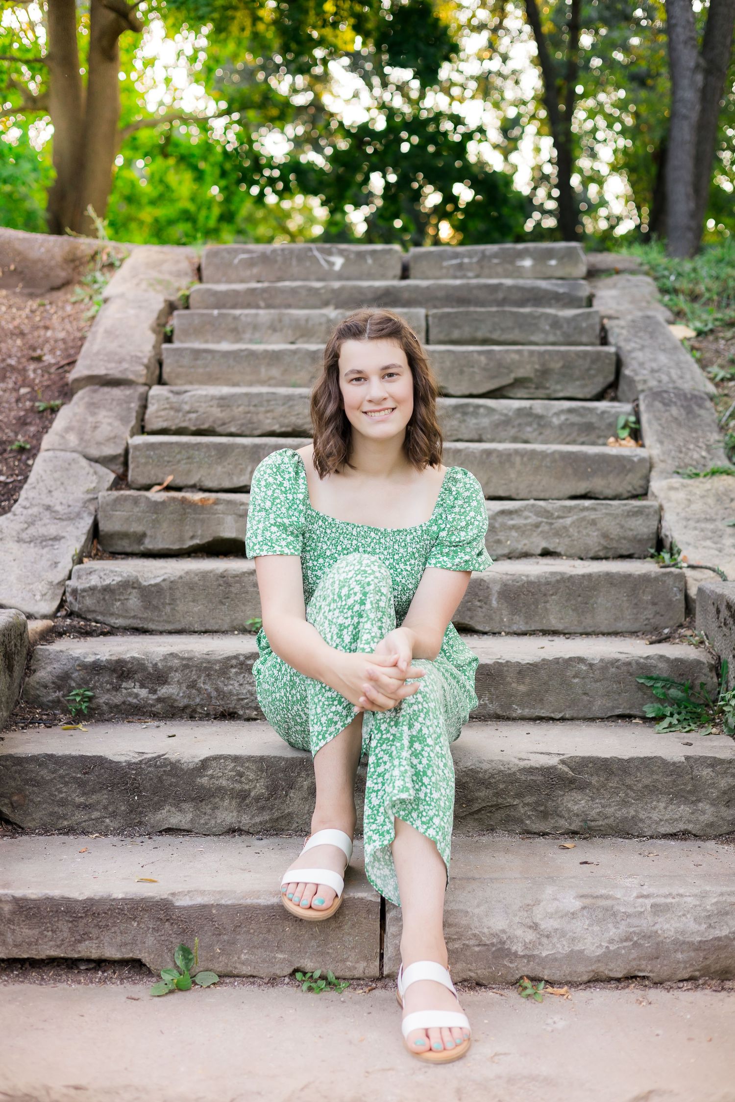 Woman in green dress sits on stone steps outdoors during summer photo session.