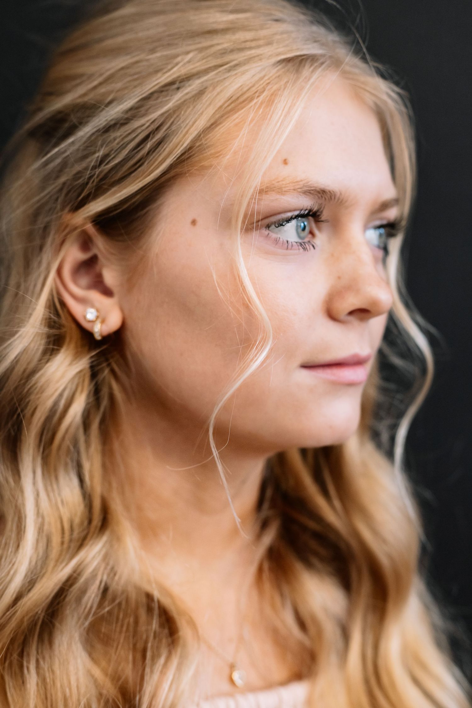 Close up profile portrait with wavy blonde hair against dark background.