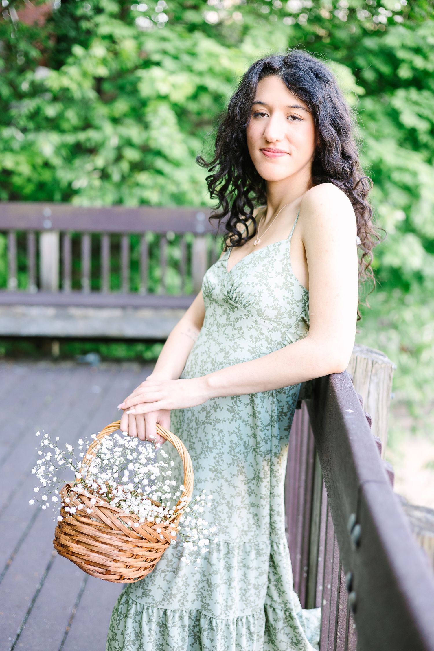 A sage green floral dress paired with a basket of baby's breath flowers on a wooden bridge walkway.