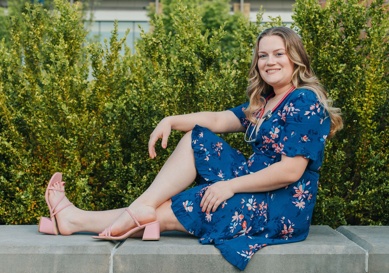 Graduate lounges in blue floral dress against garden backdrop.