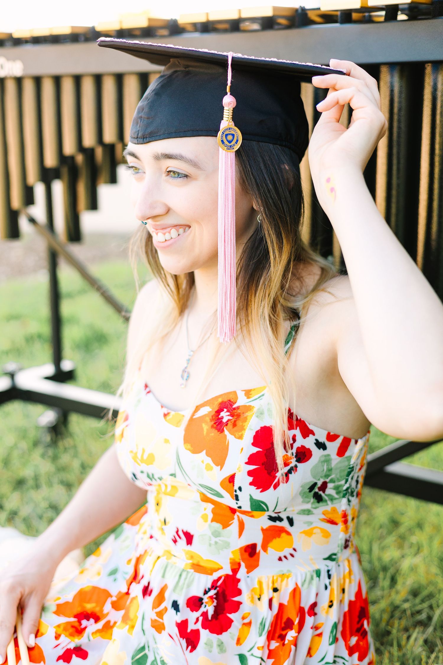 A graduate wearing a floral sundress and graduation cap poses for celebratory photos outside.