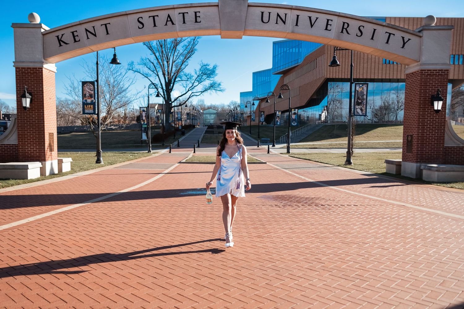 Student walking through Kent State University entrance gate on brick pathway.