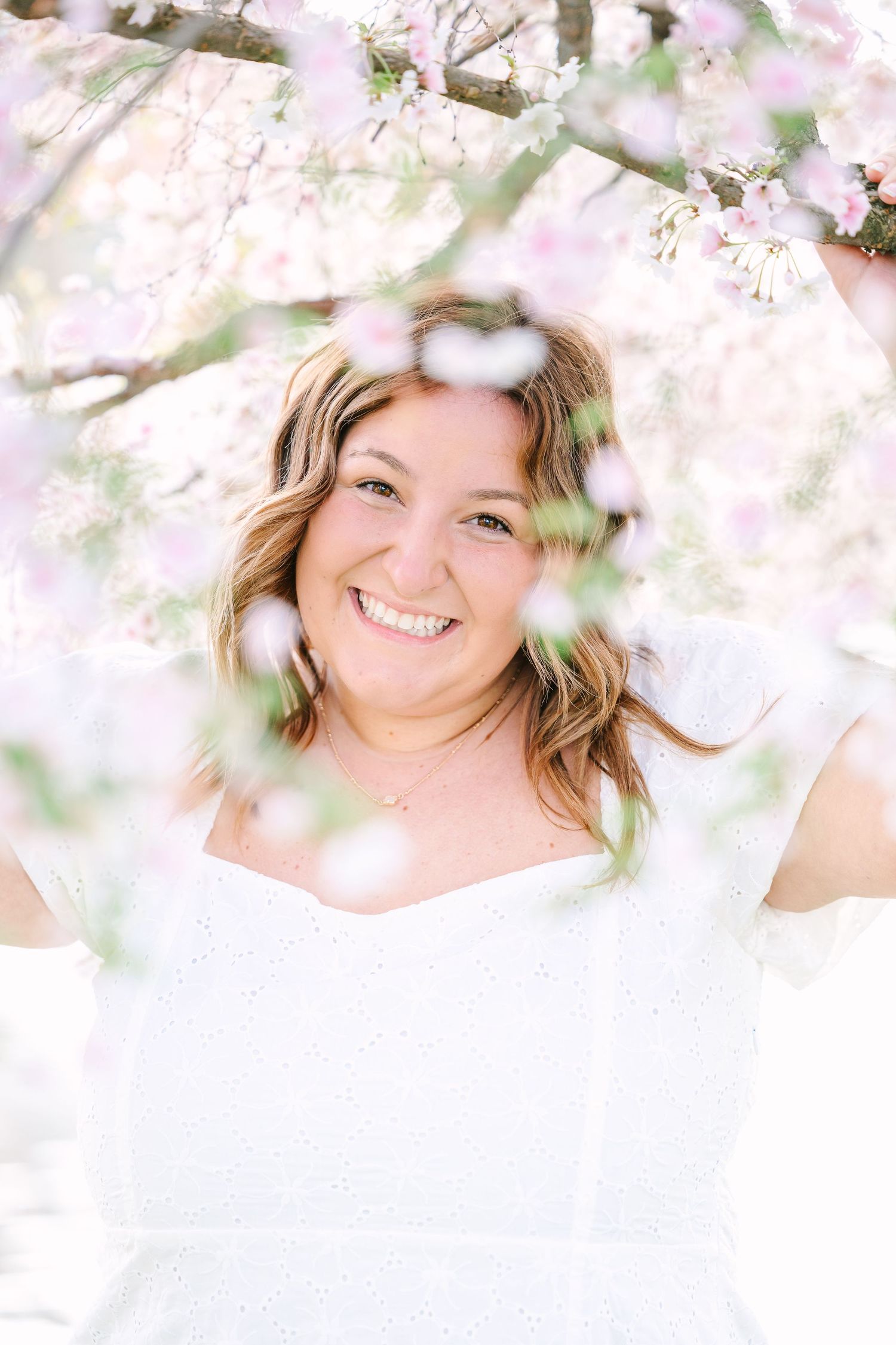 Joyful portrait surrounded by delicate white spring blossoms and soft natural lighting in ethereal outdoor setting.