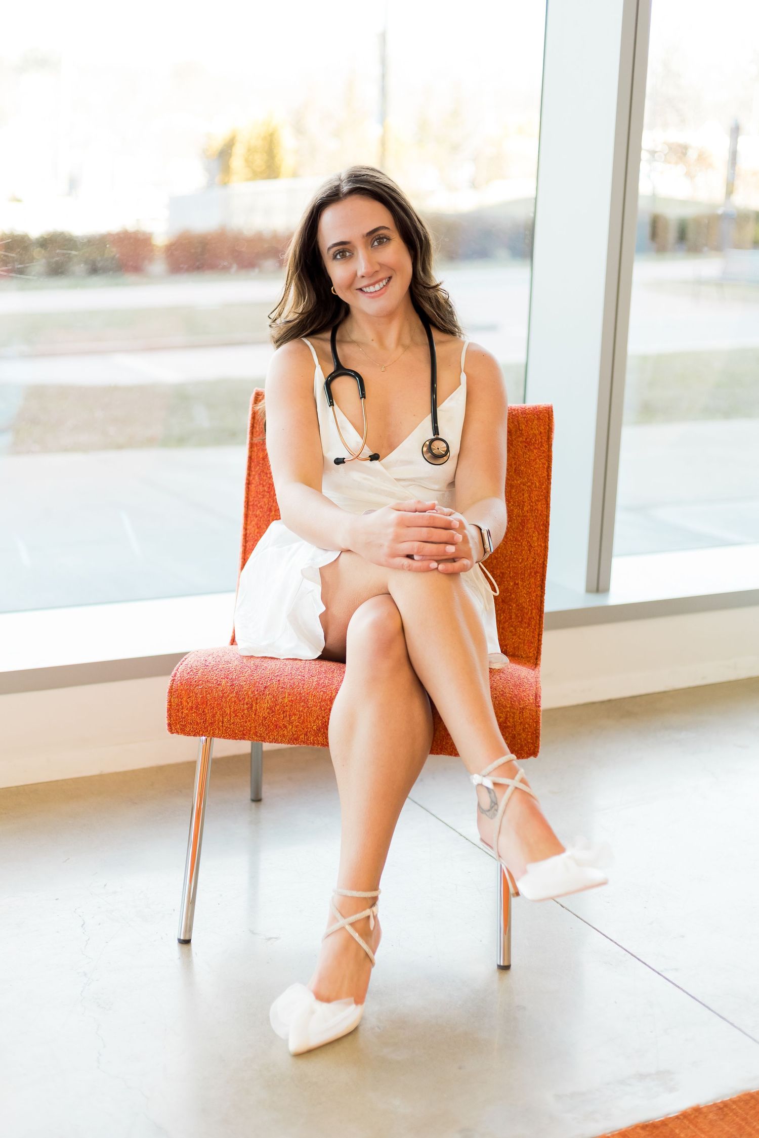 Medical graduate in white dress poses with stethoscope in modern office setting.