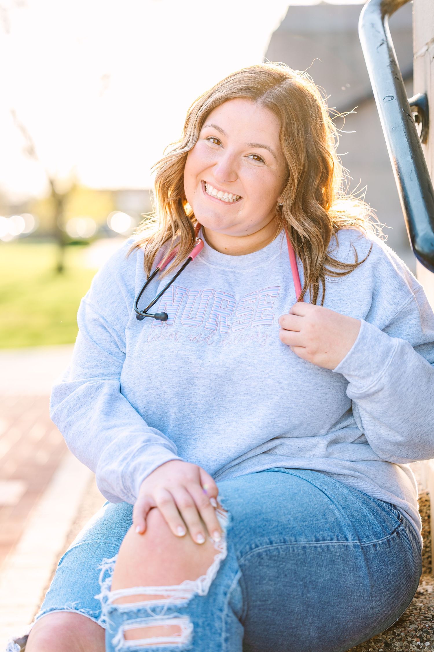 A pregnant woman in a gray sweatshirt and jeans poses during a sunset maternity photoshoot outdoors.