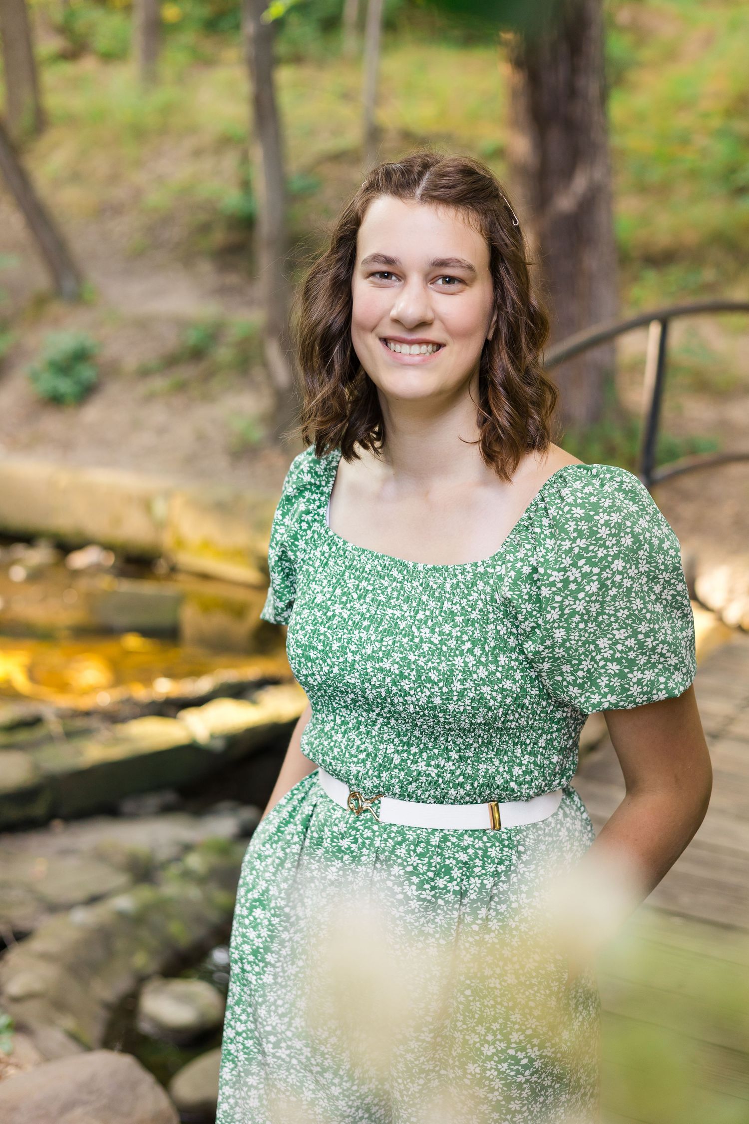 Woman wearing a green floral dress stands outdoors on a wooden boardwalk.