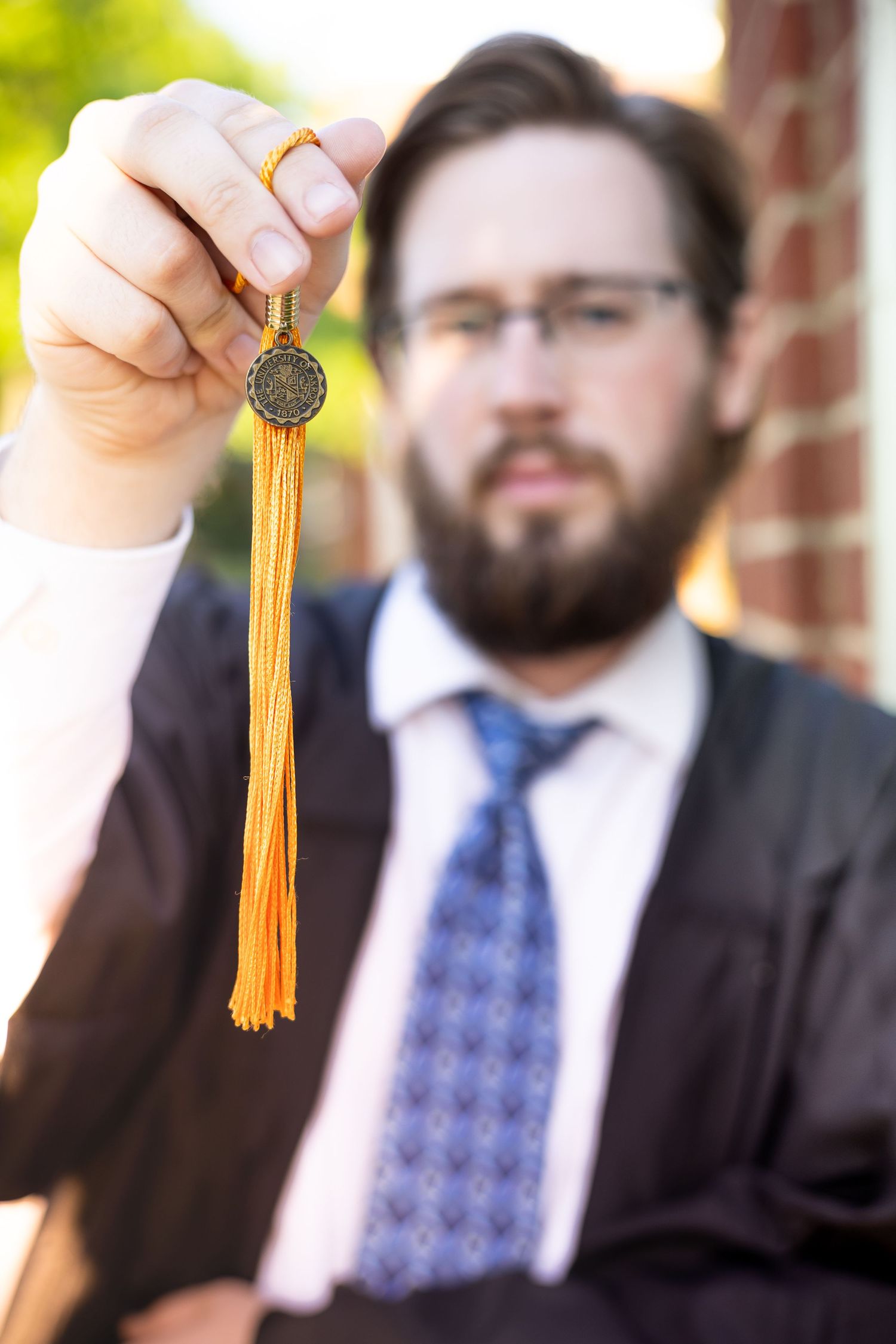Graduate holds up orange and gold graduation tassel against brick building backdrop.