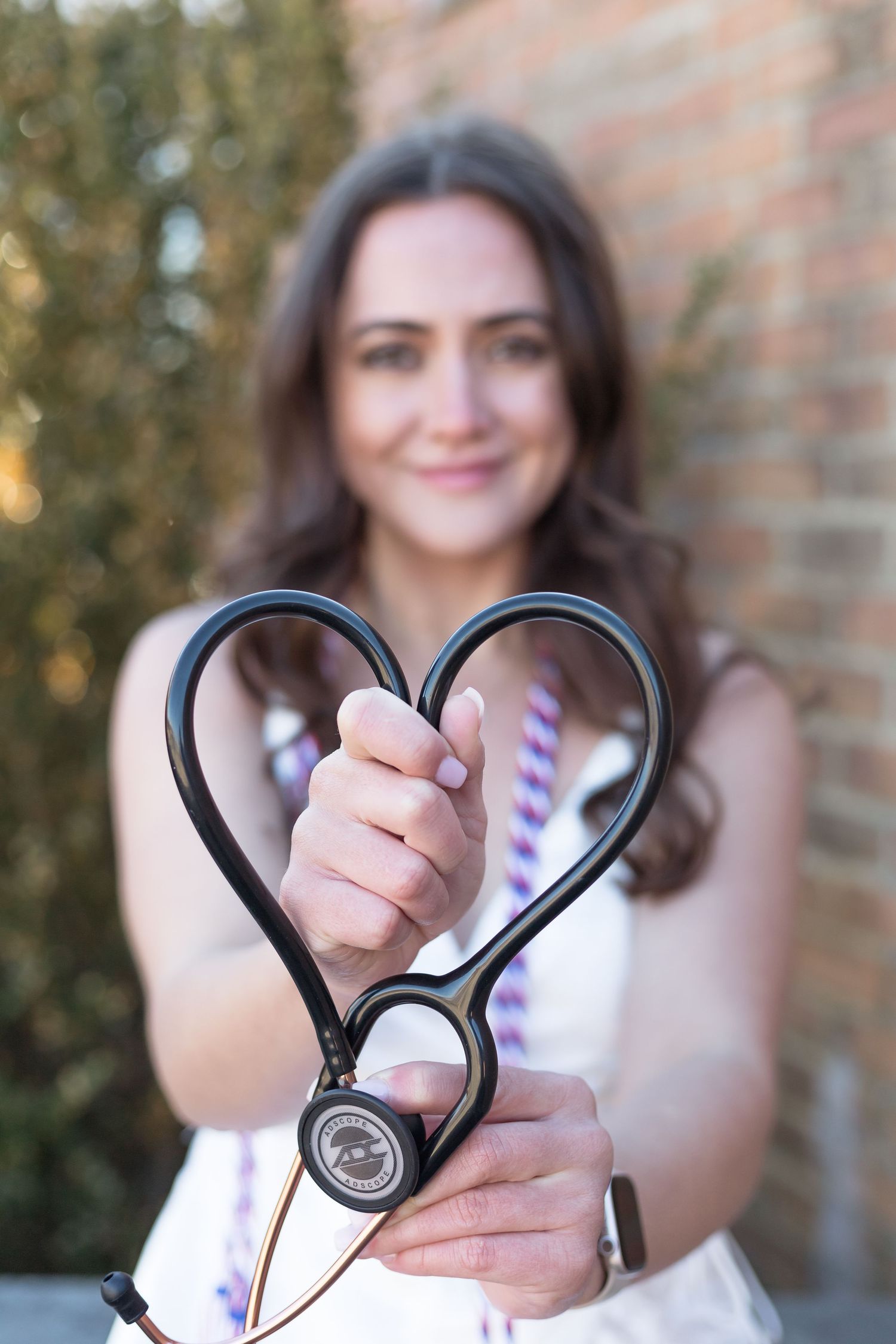 Medical professional holds stethoscope shaped like heart during graduation photos.