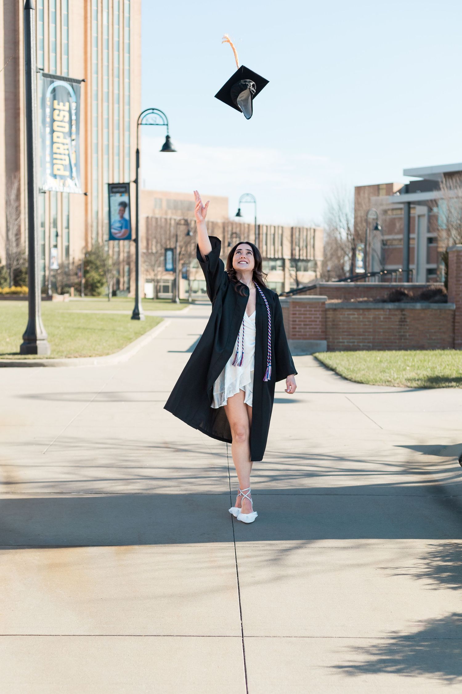Graduate in black gown throws cap in air during celebratory graduation photo.