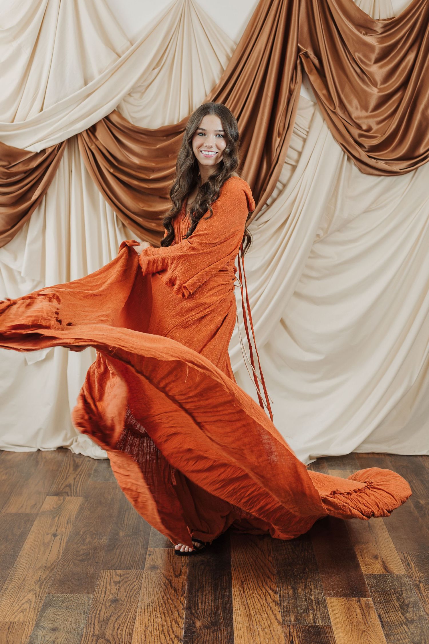 Flowing orange dress with dramatic movement captured against draped fabric backdrop.