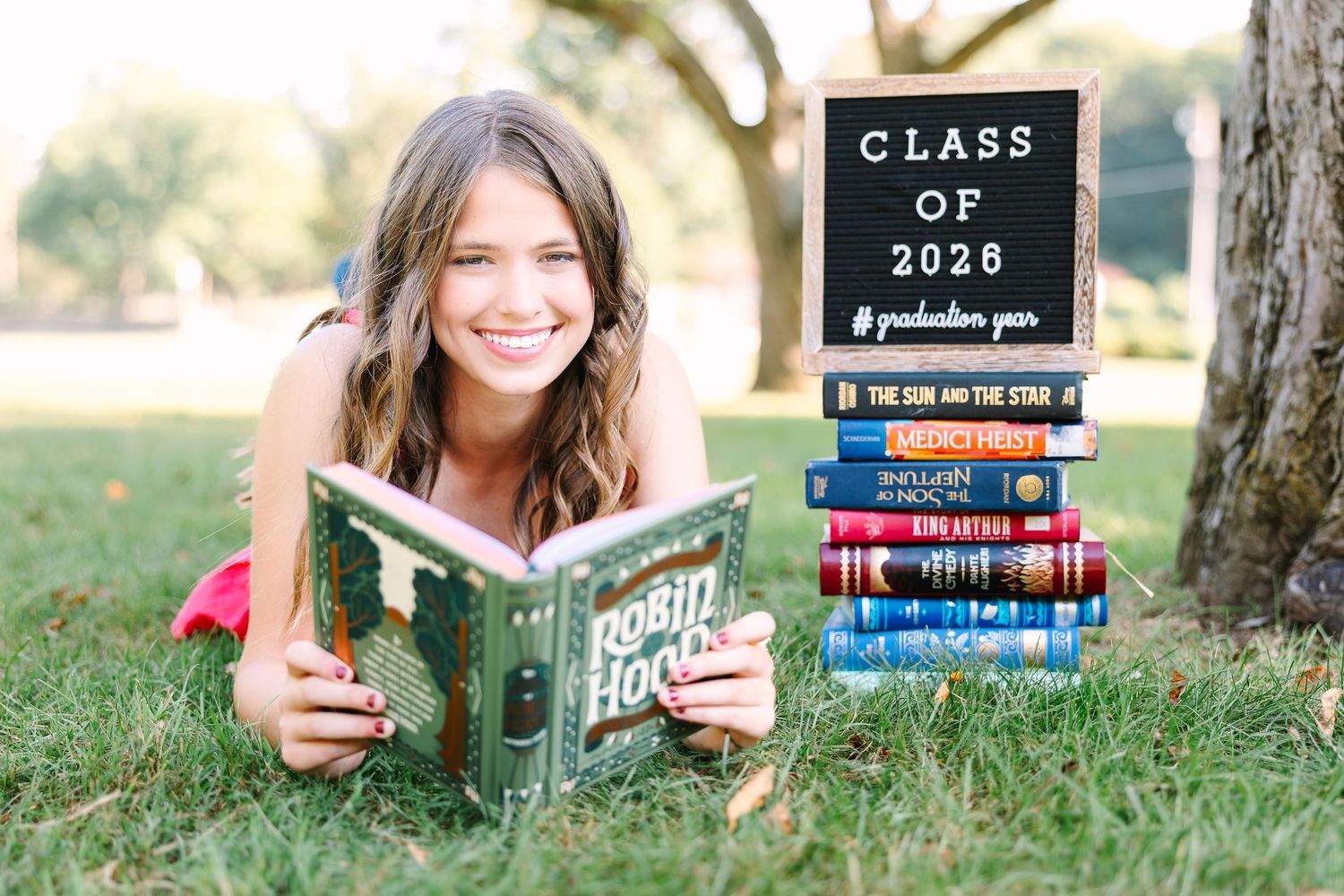 A series of graduation photos show textbooks and diploma props arranged outdoors in grass with a Class of 2020 sign.
