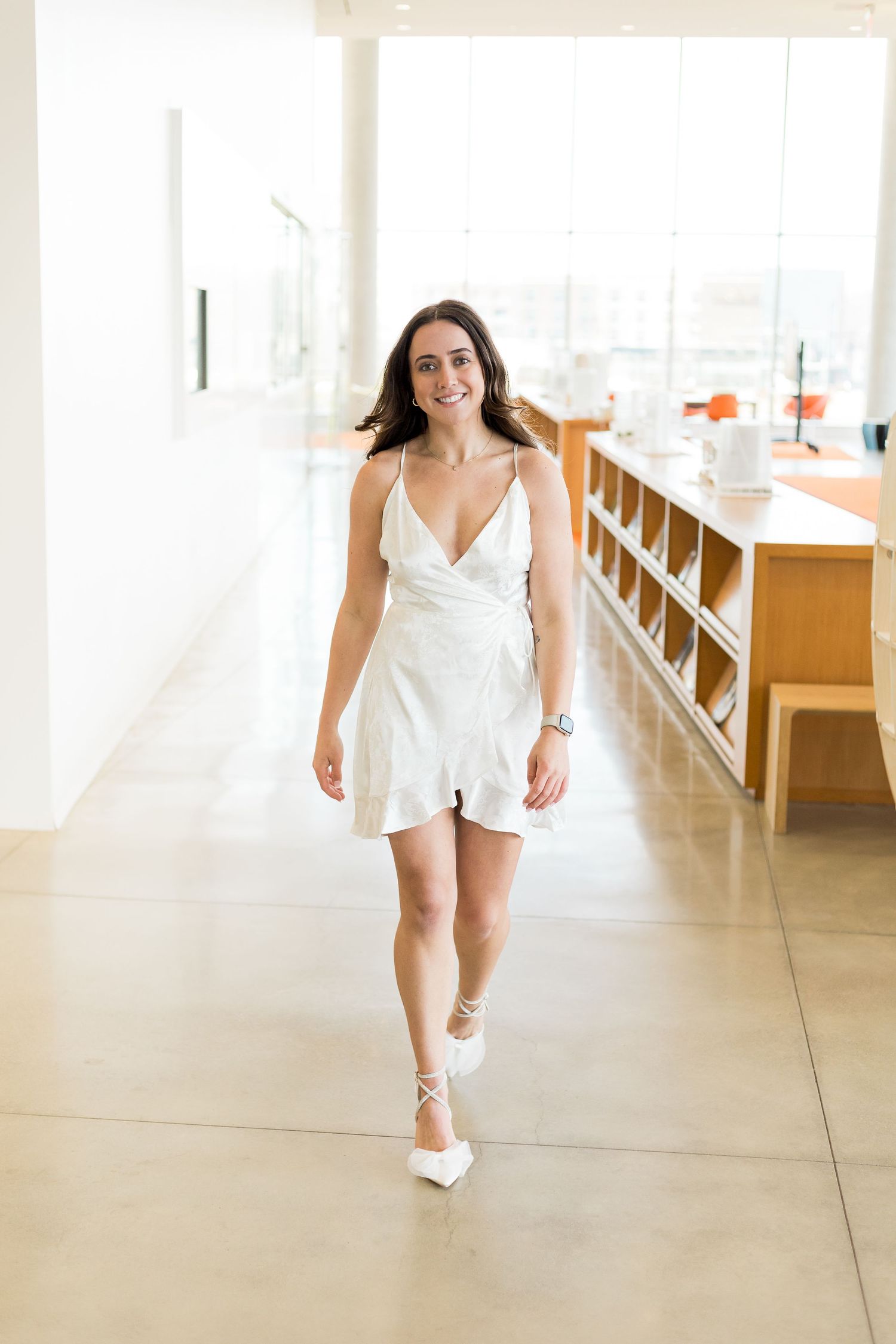 Woman in white sundress walking down hallway in bright modern interior space.
