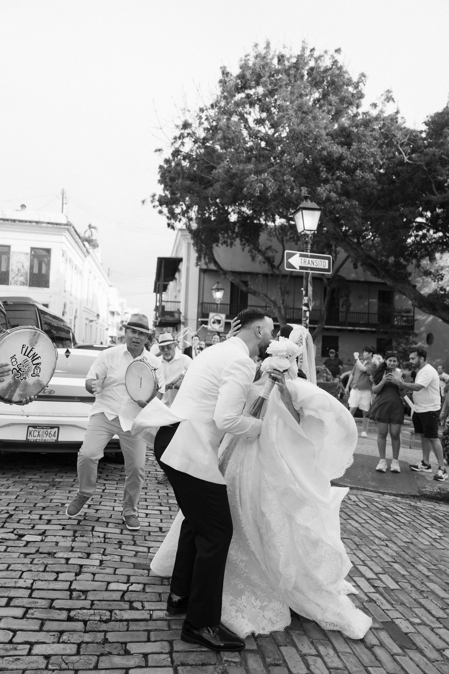 Black and white photo of groom dipping bride on cobblestone street with band playing nearby.
