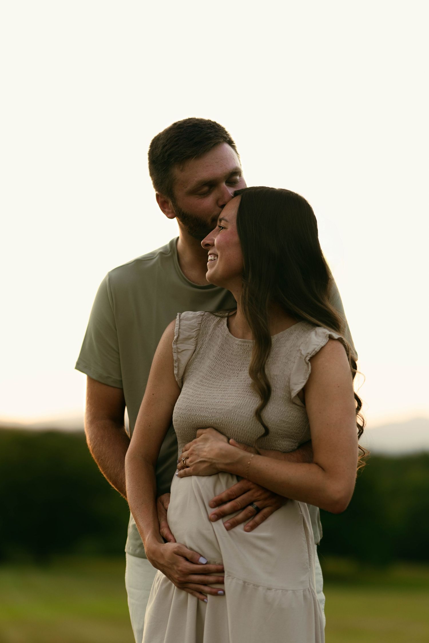Intimate moment between couple during sunset pregnancy photoshoot.