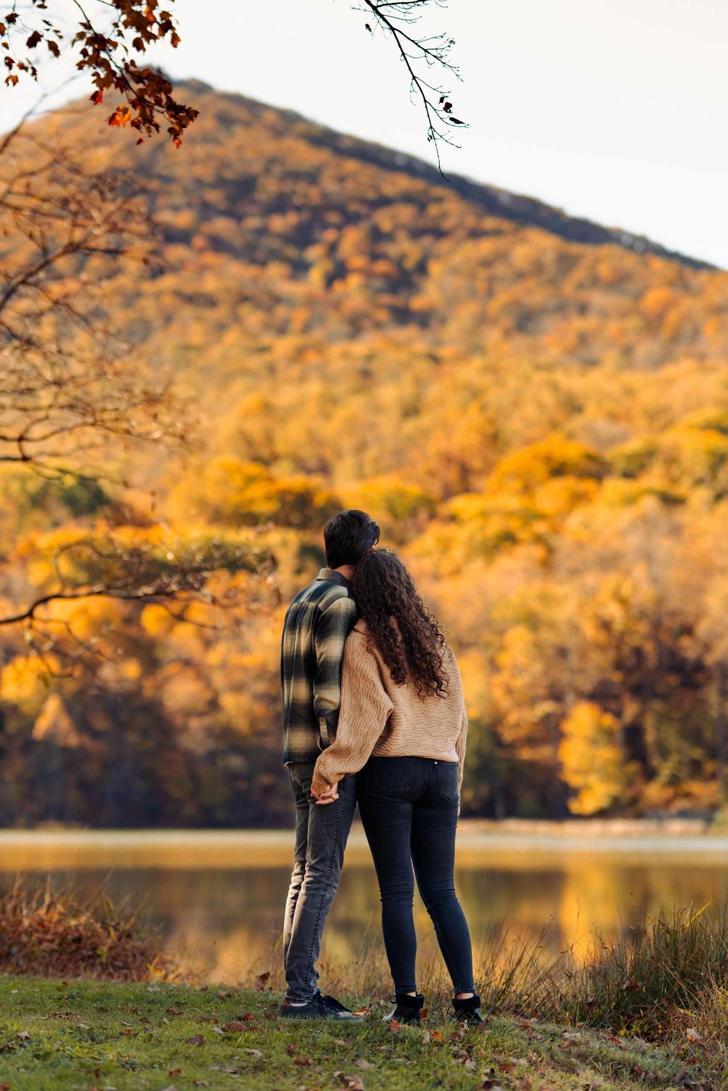 A couple embraces by a scenic lake with autumn mountains in the background.