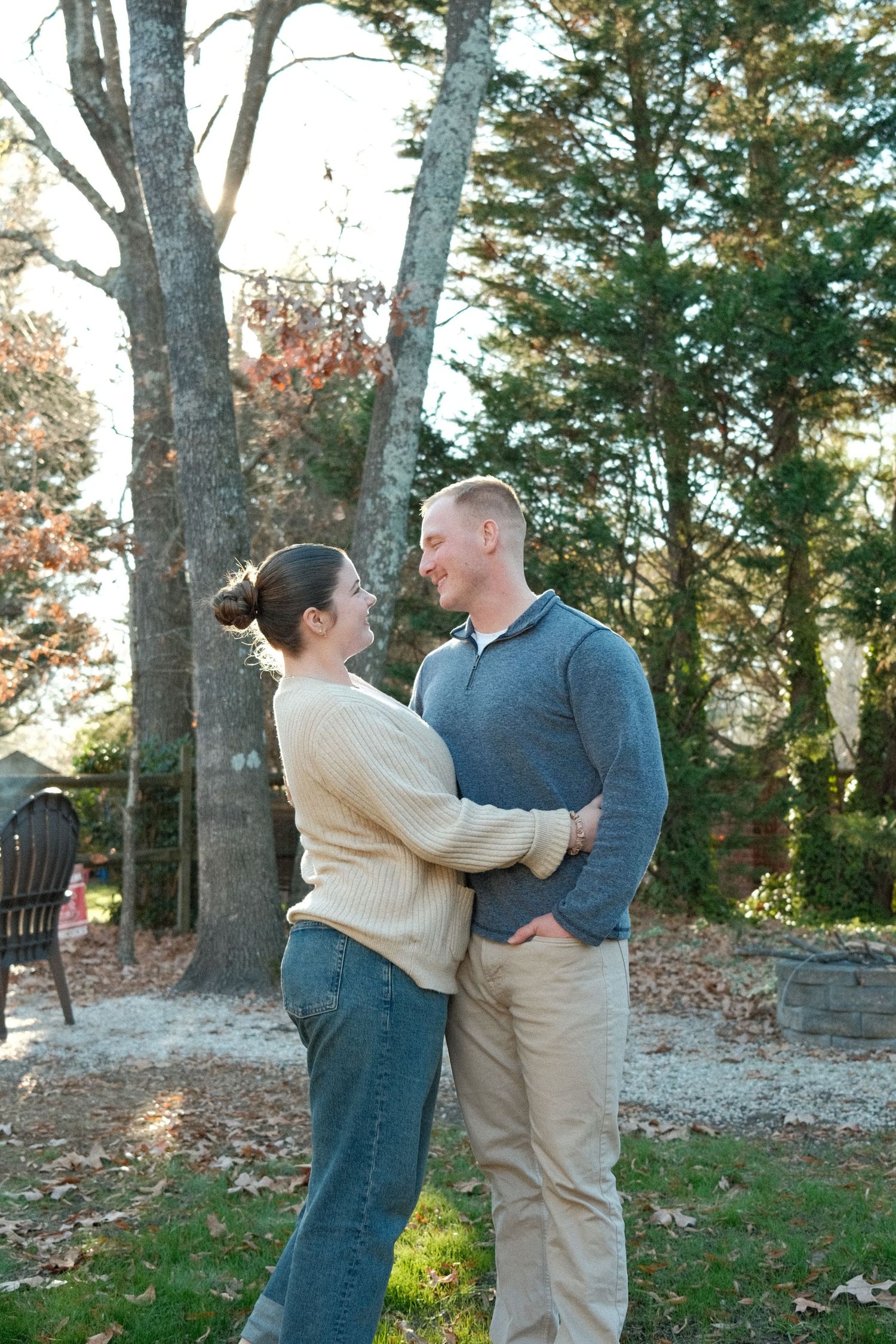 A couple embracing in a park with trees and foliage in the background.